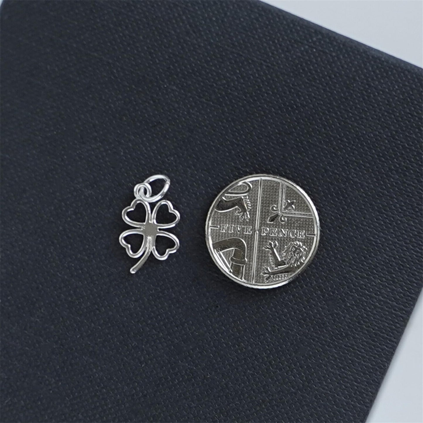 Four-leaf clover charm in silver metal, shown with coin for scale