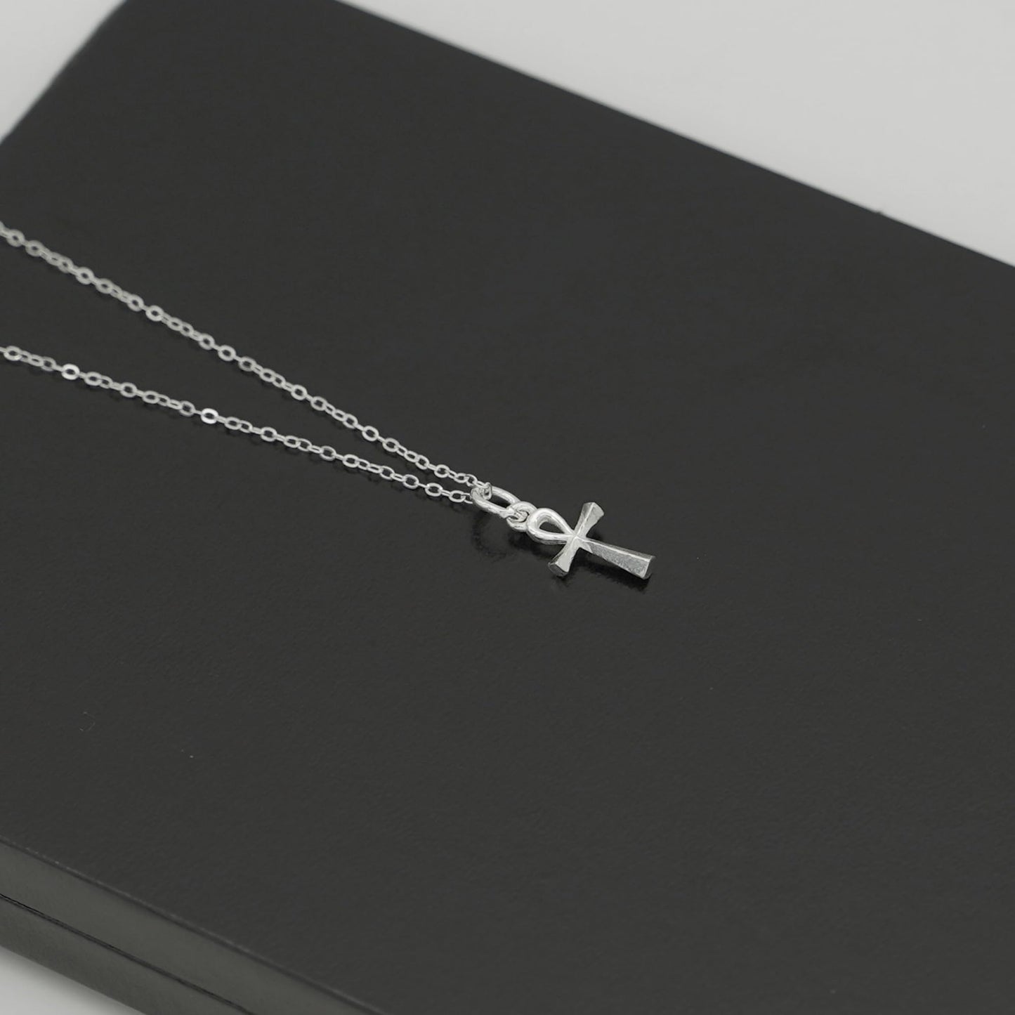 Ankh cross pendant on silver-tone chain necklace, angled close-up.