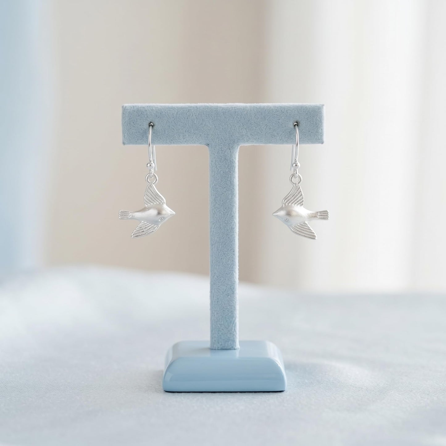 Silver dangling flying bird earrings on display stand