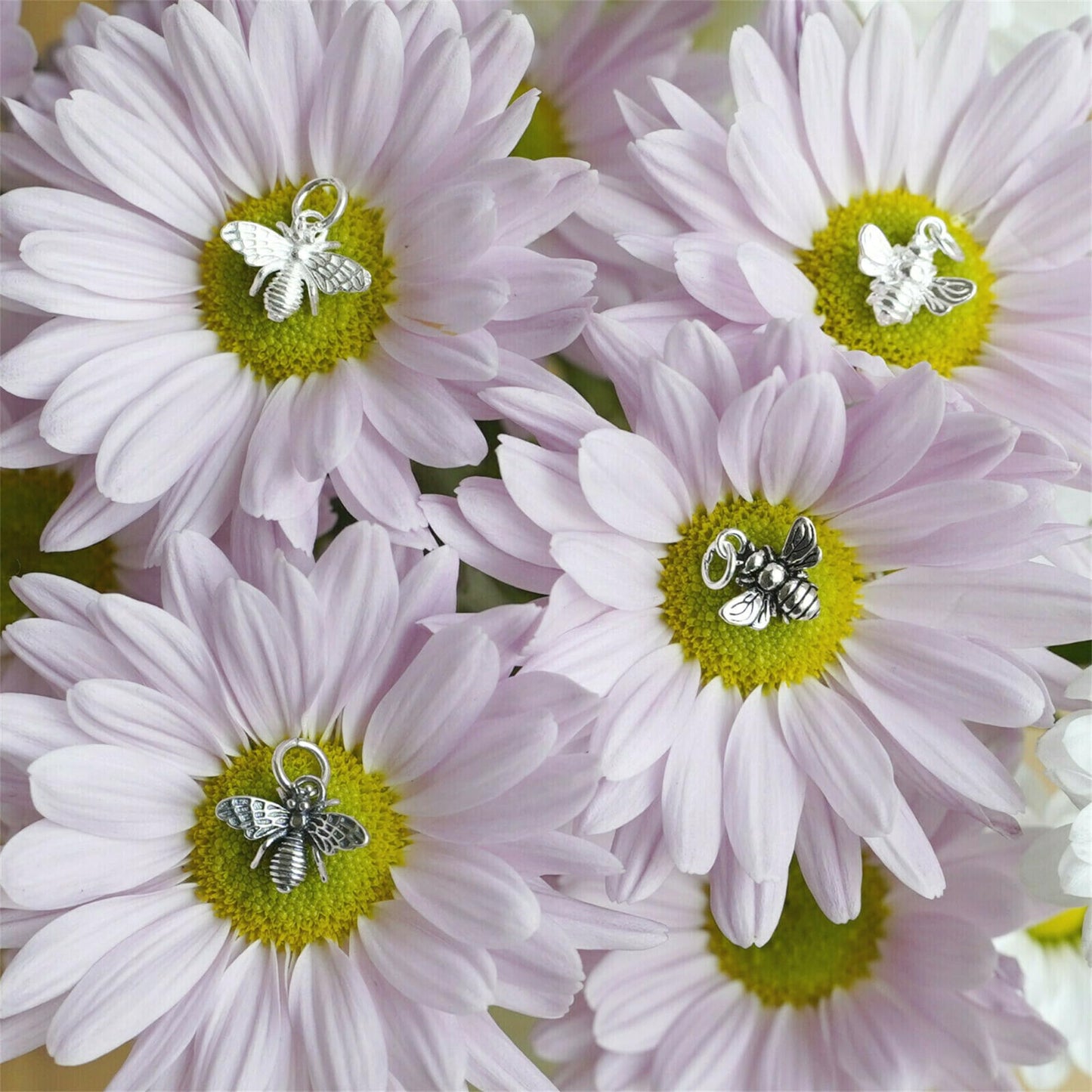 Multiple silver bee charm pendants with wings on white daisies