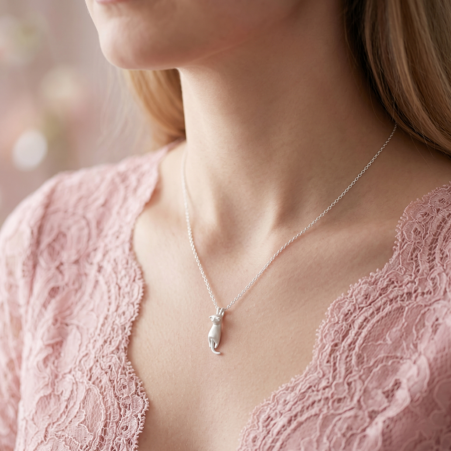 Silver cat pendant necklace worn on pink lace top, chain and charm