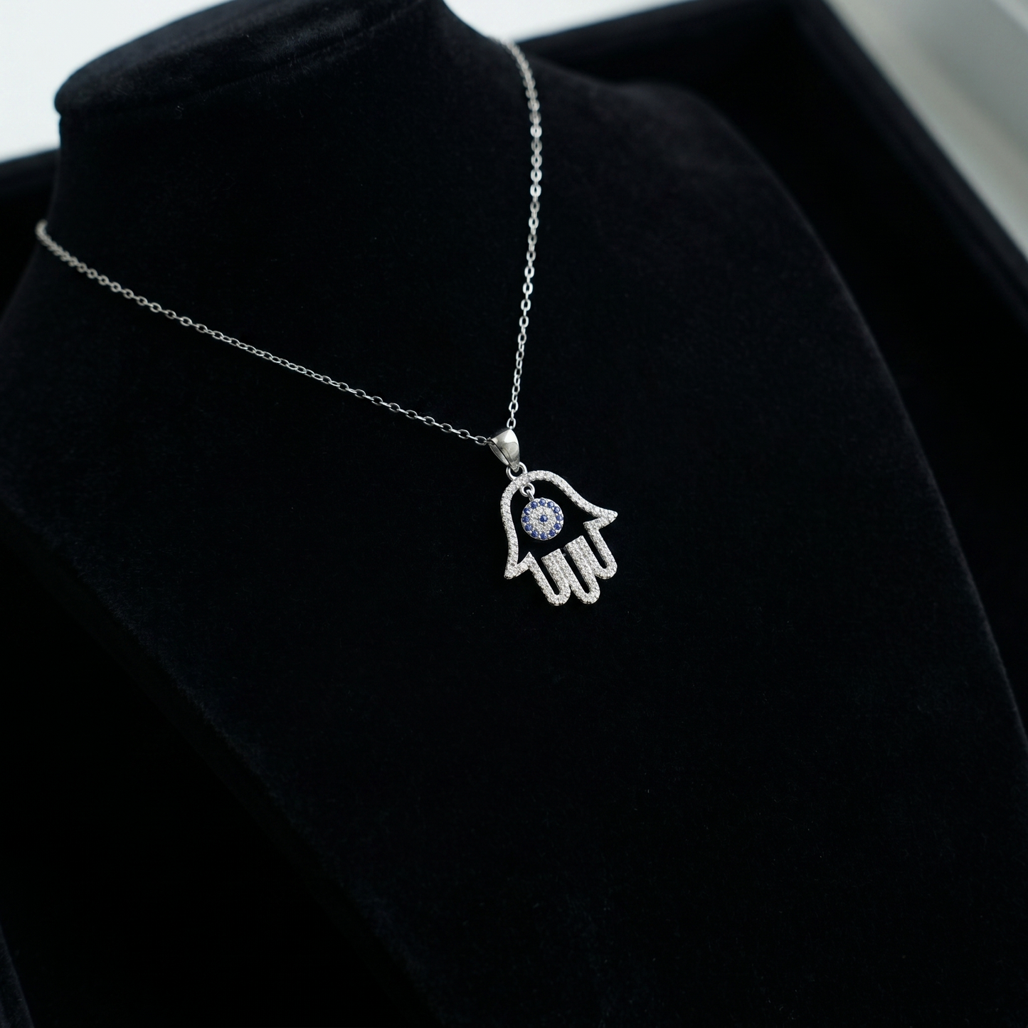 Hamsa hand pendant with blue eye stone hanging on silver chain
