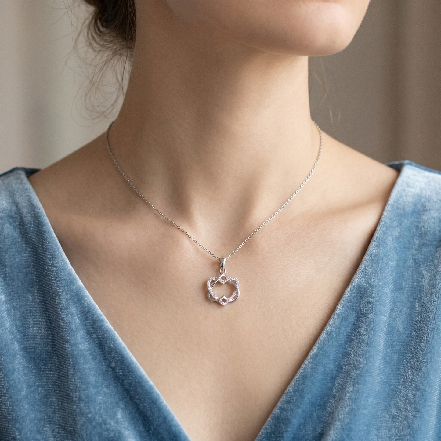 Silver heart knot pendant necklace worn on a neckline with fine chain and stones.