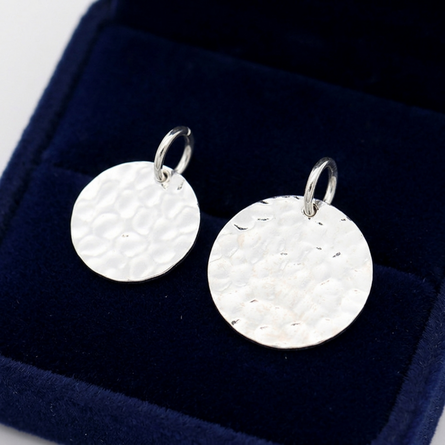 Pair of silver-tone round embossed disc charms with hanging loops on cushion