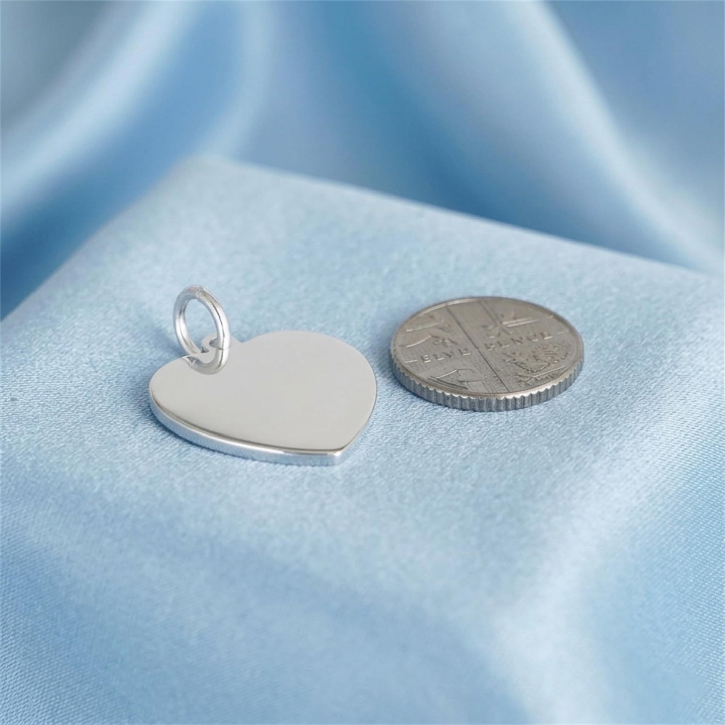 Heart pendant with polished silver loop, smooth white heart face beside coin for scale