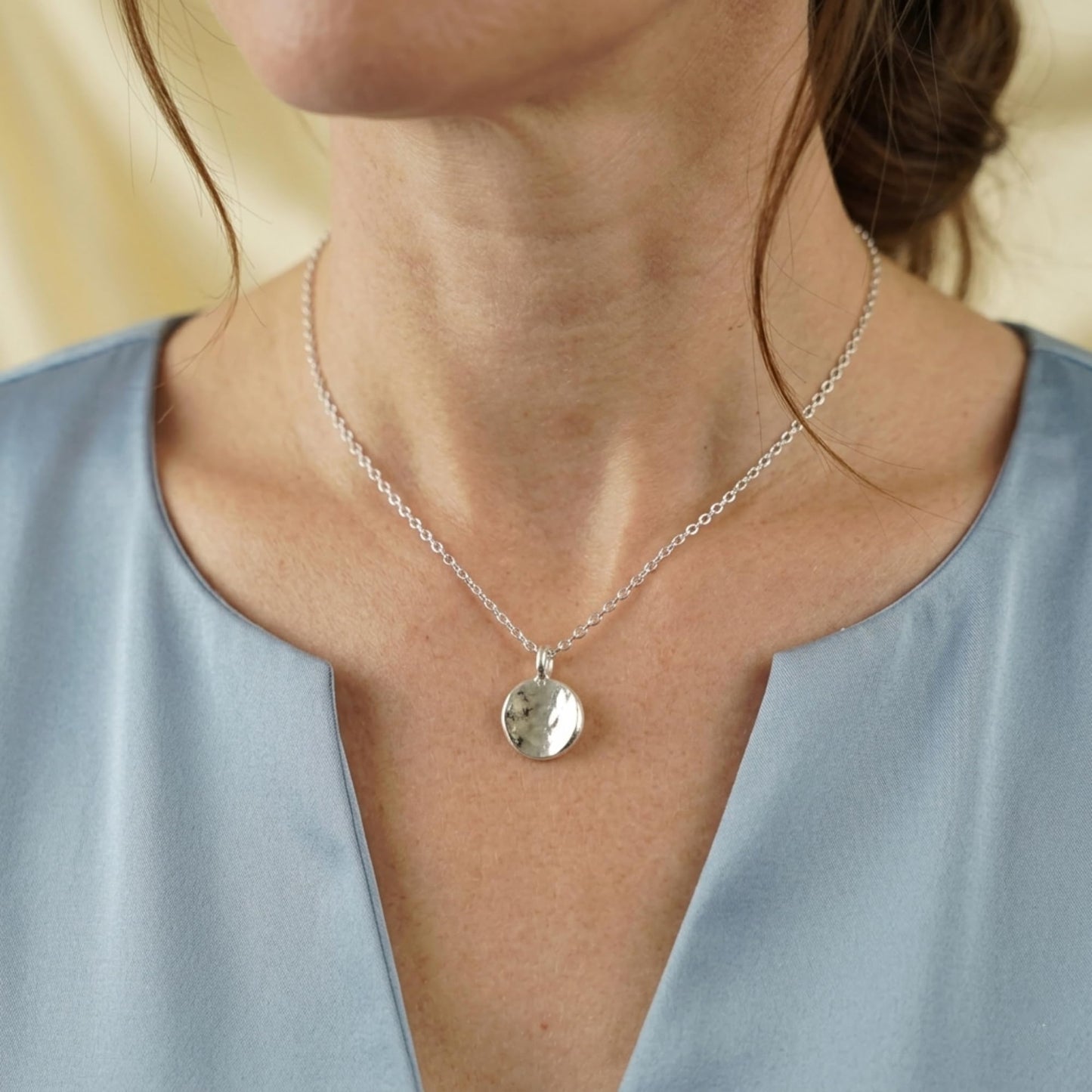 Organic hammered disc pendant on a necklace, silver-tone disc charm centered on chest