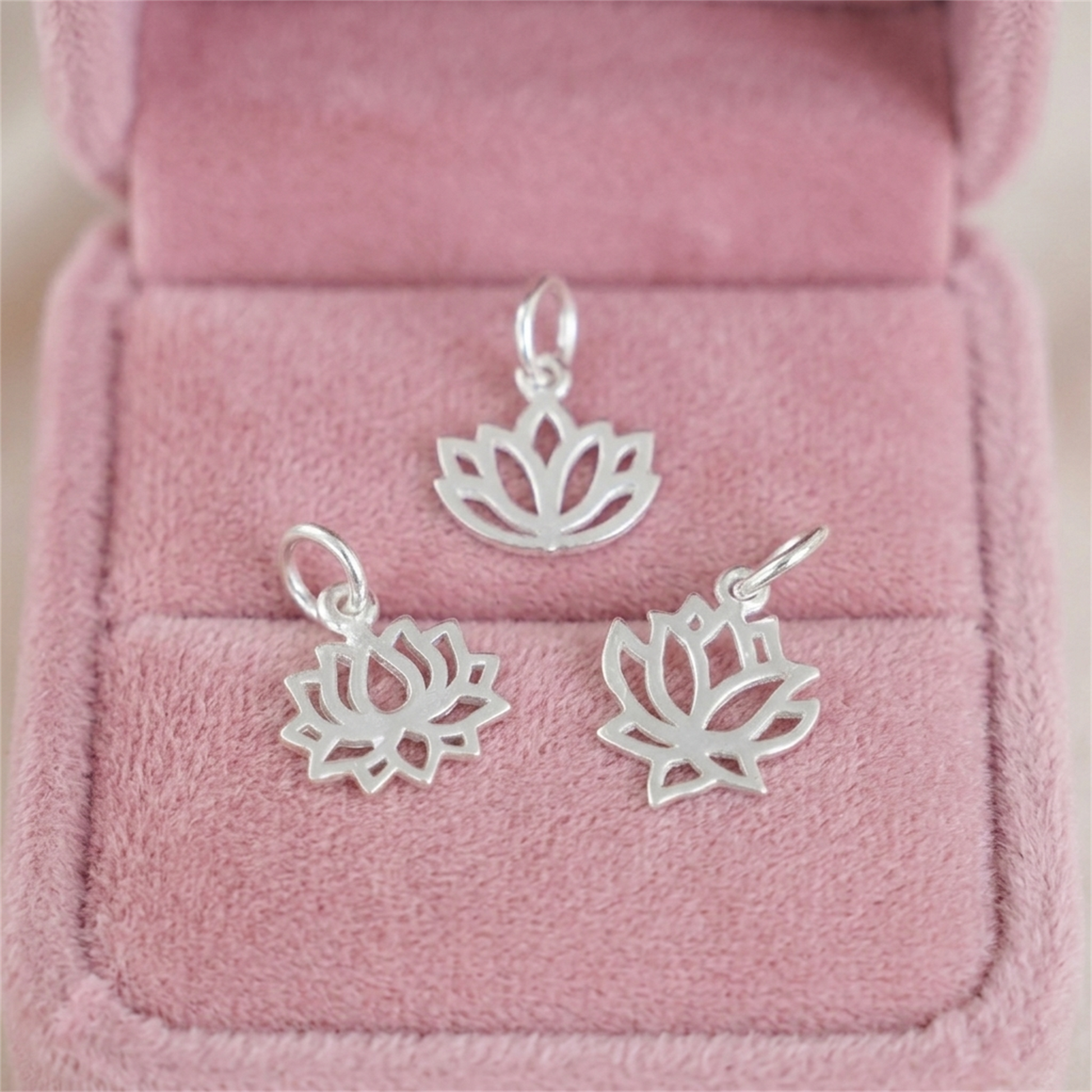 Set of small filigree lotus charm pendants with metal rings and hooks on display