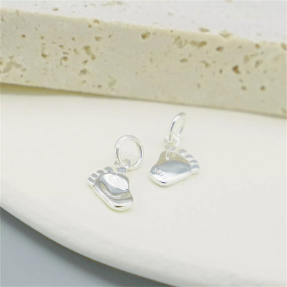 Silver baby foot charm pair with hanging loops and light blue enamel soles