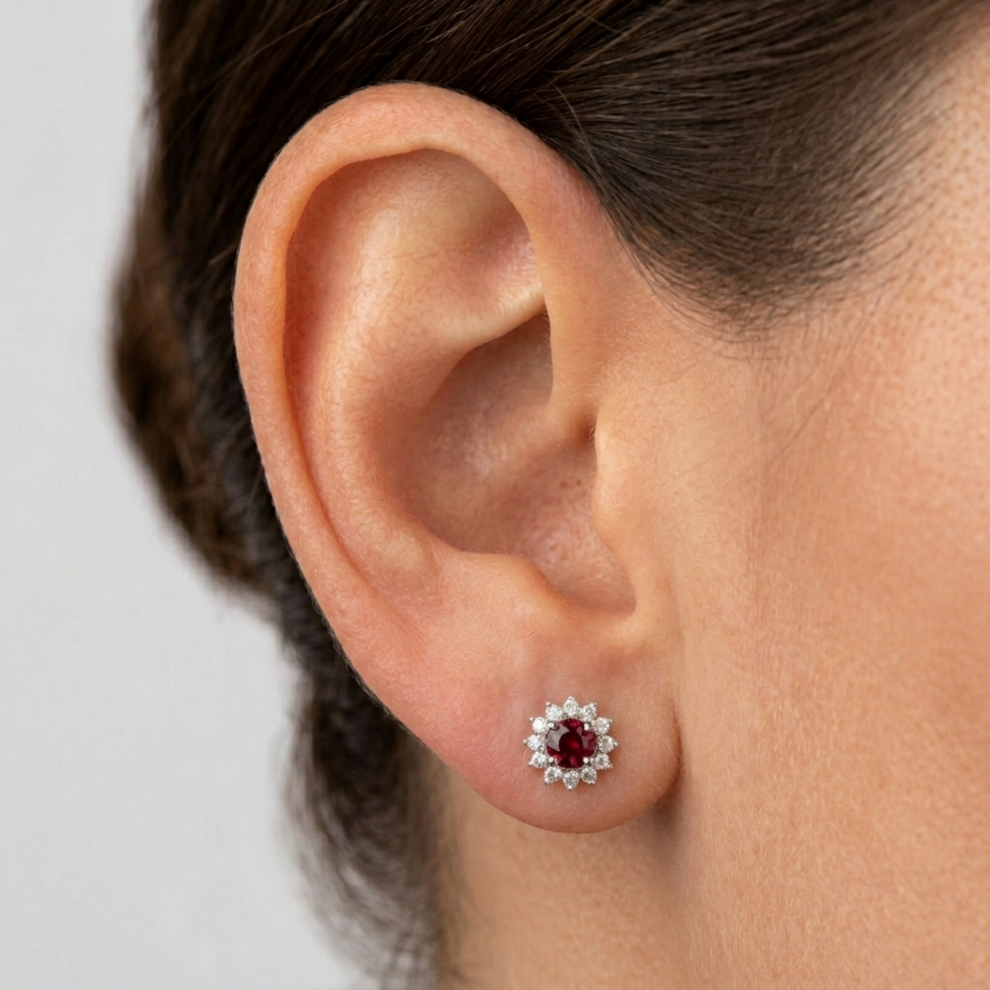 Red round gemstone stud earrings with halo cluster worn on ear