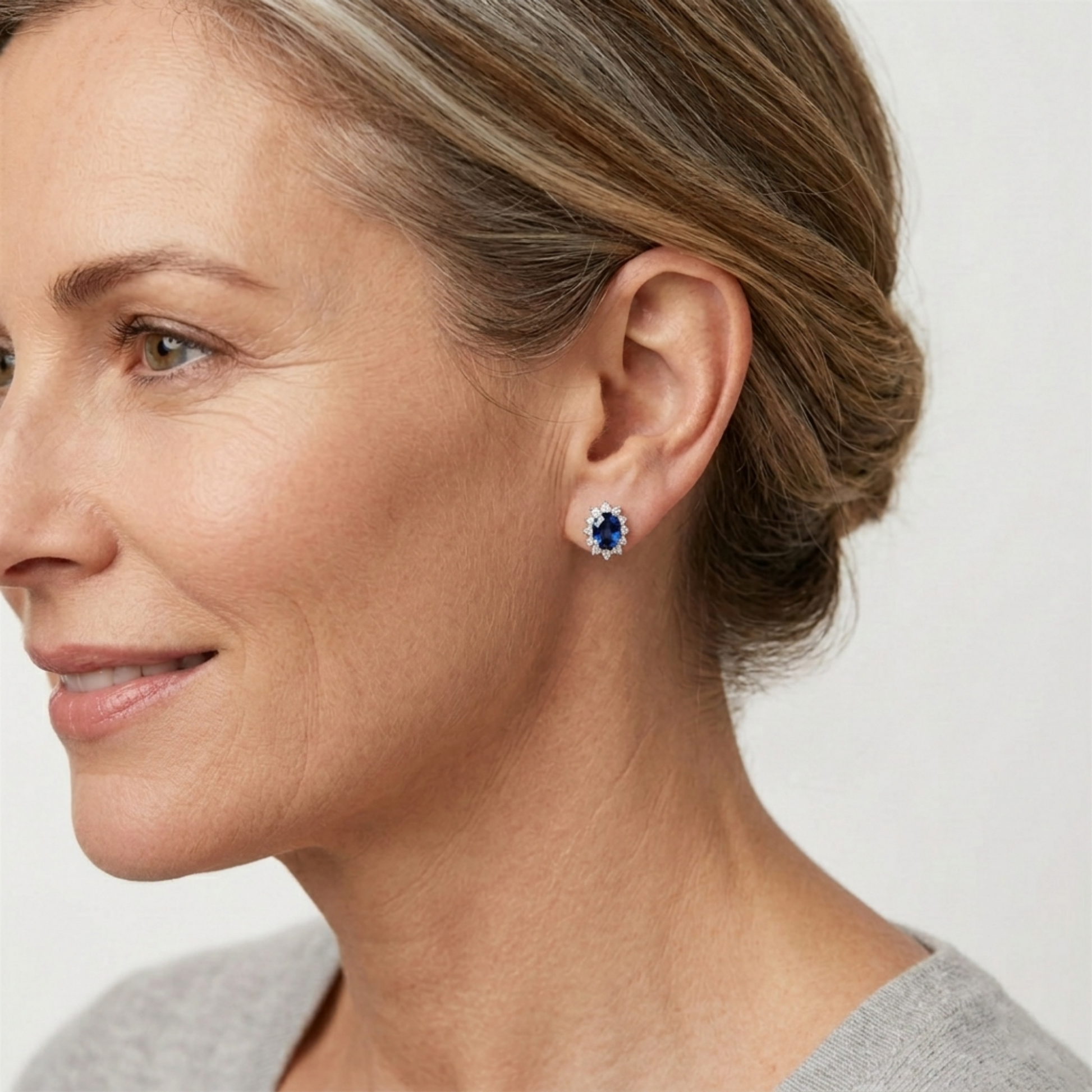 Woman wearing oval sapphire cluster stud earrings with white stone halo