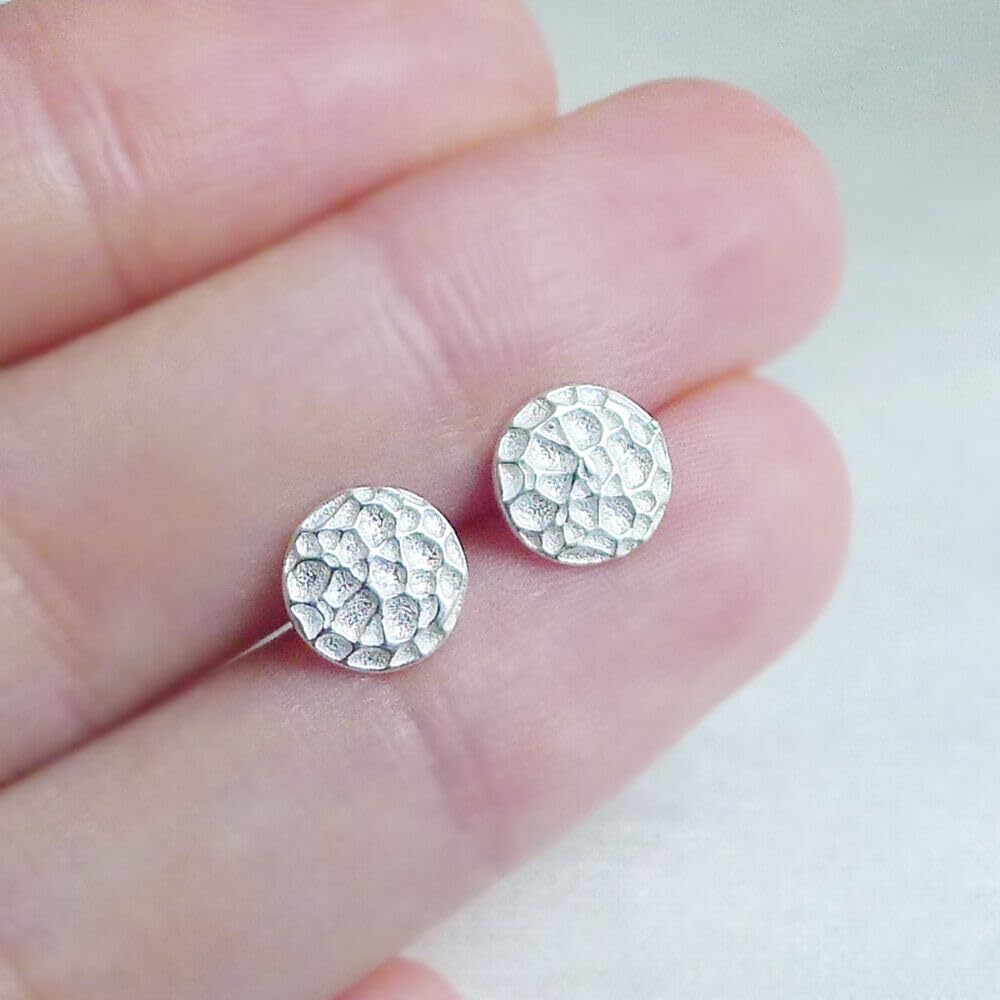 Hammered disc stud earrings held in fingers, textured round silver-tone pair