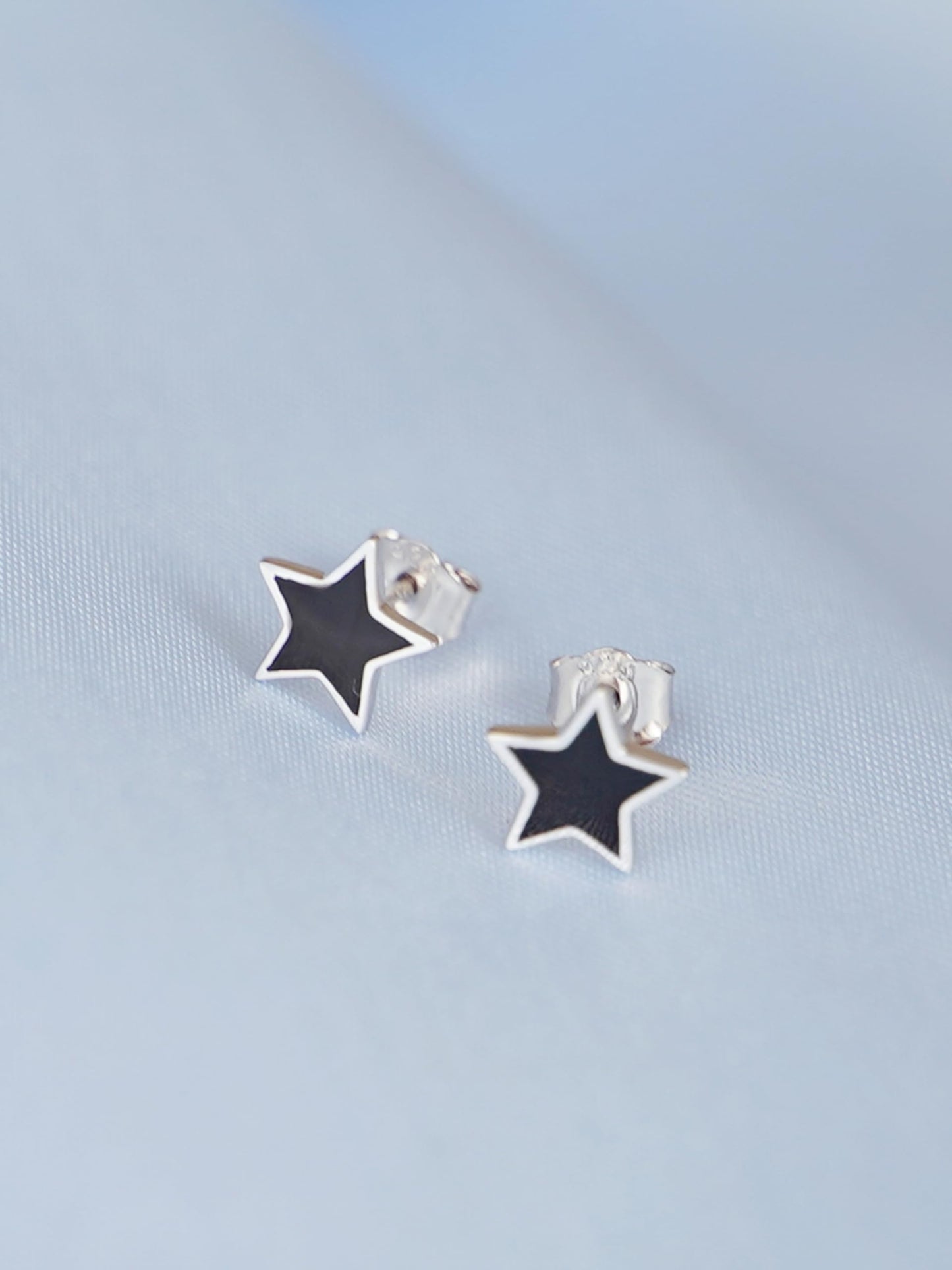 Black star studs with silver back, close-up of black enamel and metal post