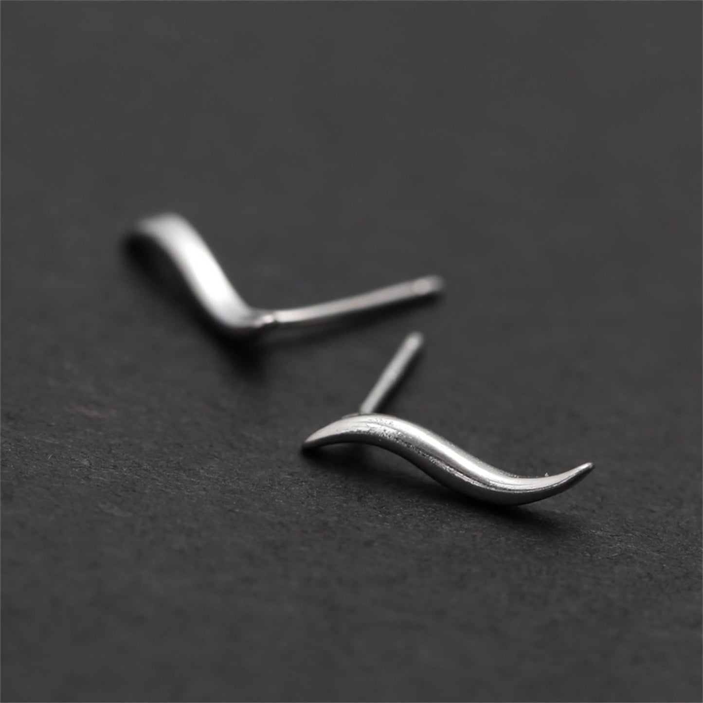Wavy vine climber stud earrings, soft focus close-up of curved wave silhouette