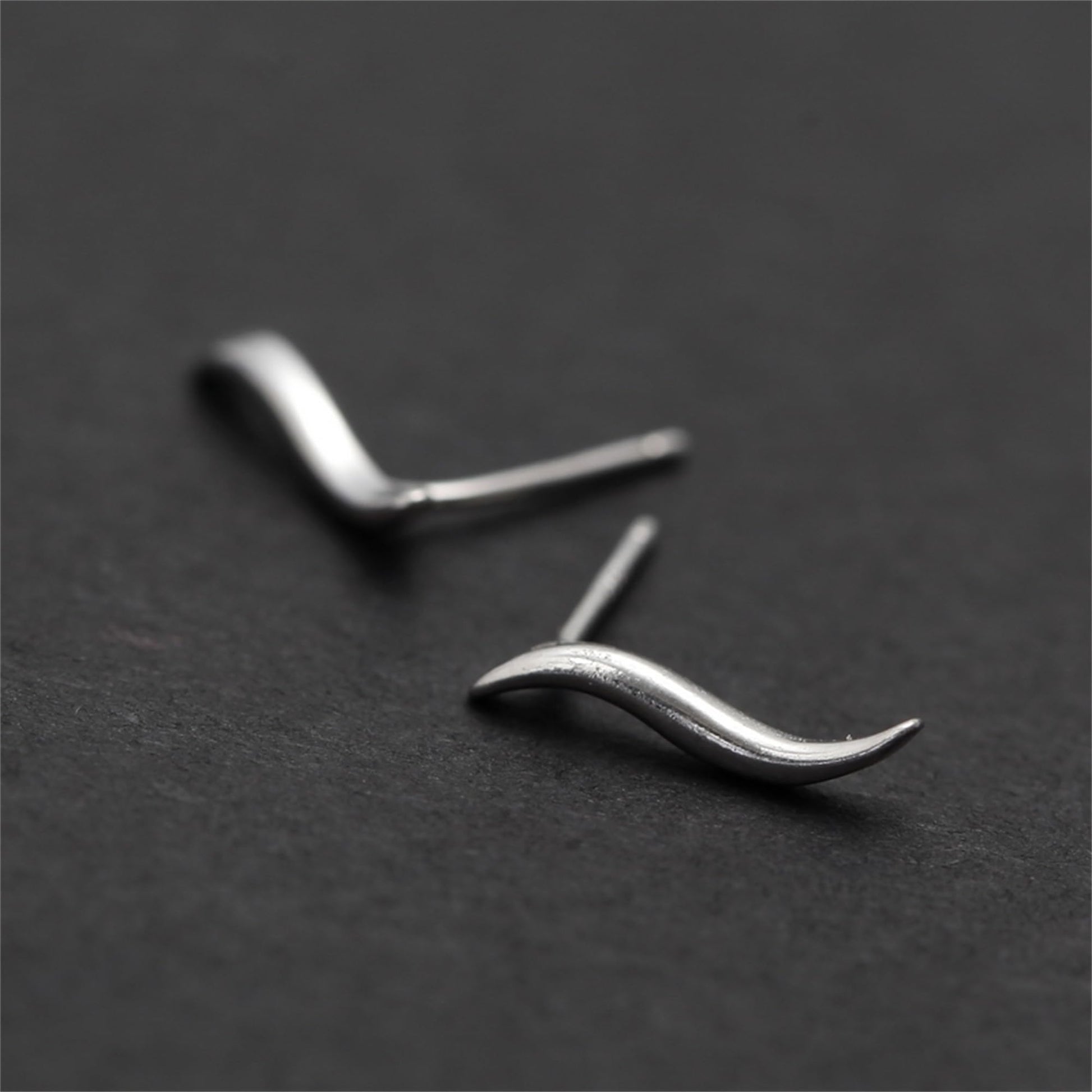 Wavy vine climber stud earrings, soft focus close-up of curved wave silhouette