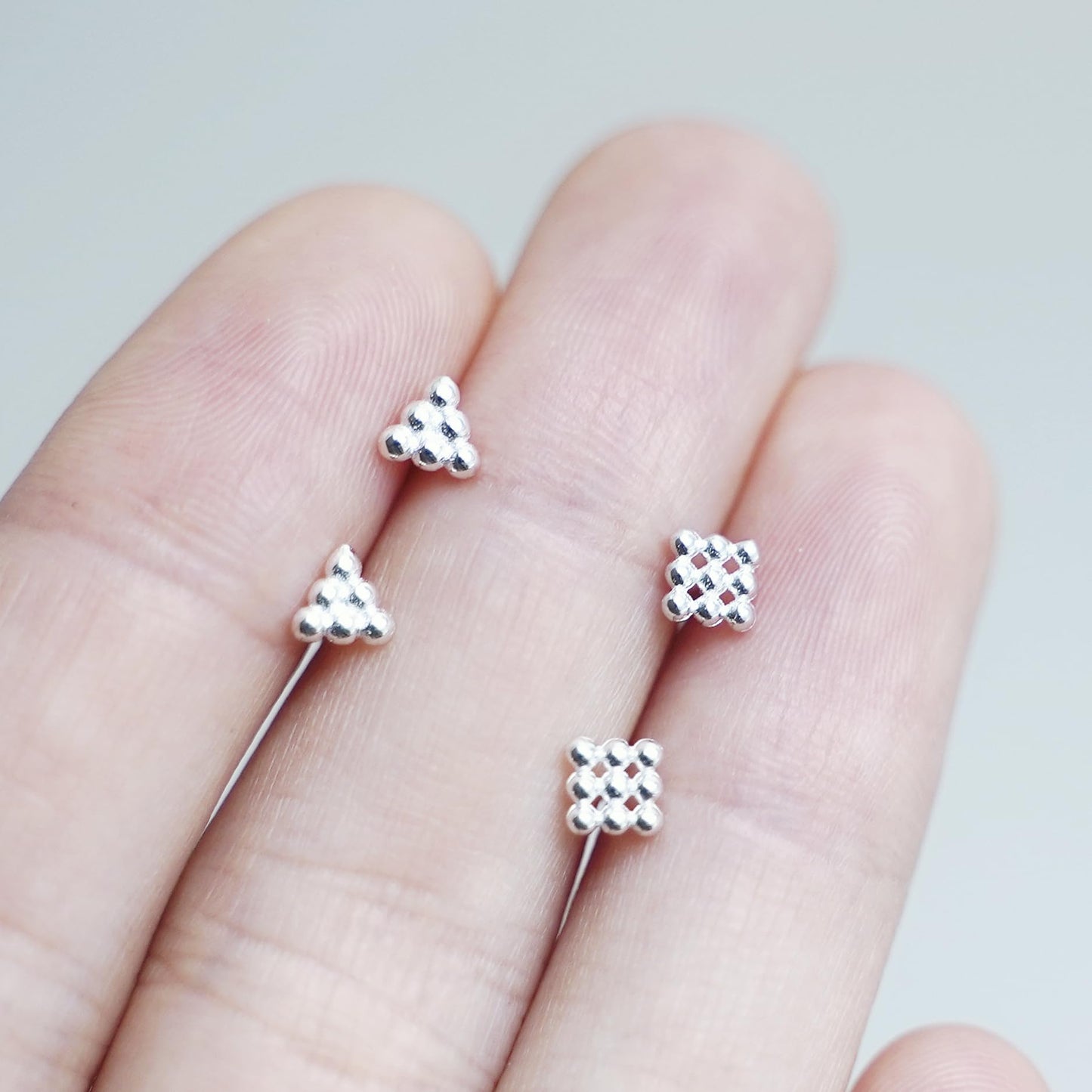 Mini geometric stud earrings on fingers: tiny cube and triangle designs