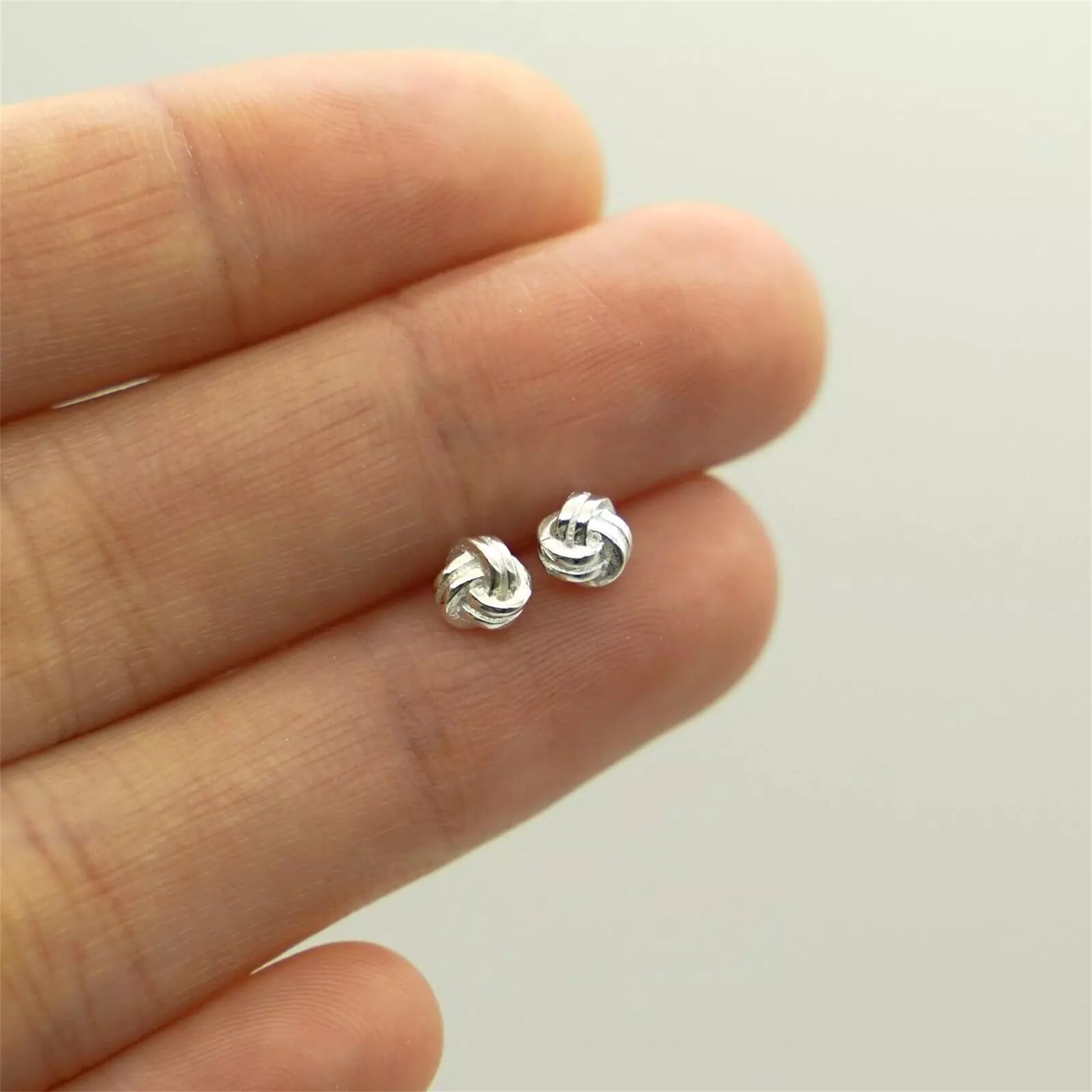 Mini Love Knot Ohrstecker in der Hand, silberfarbenes Knotendesign im Nahblick