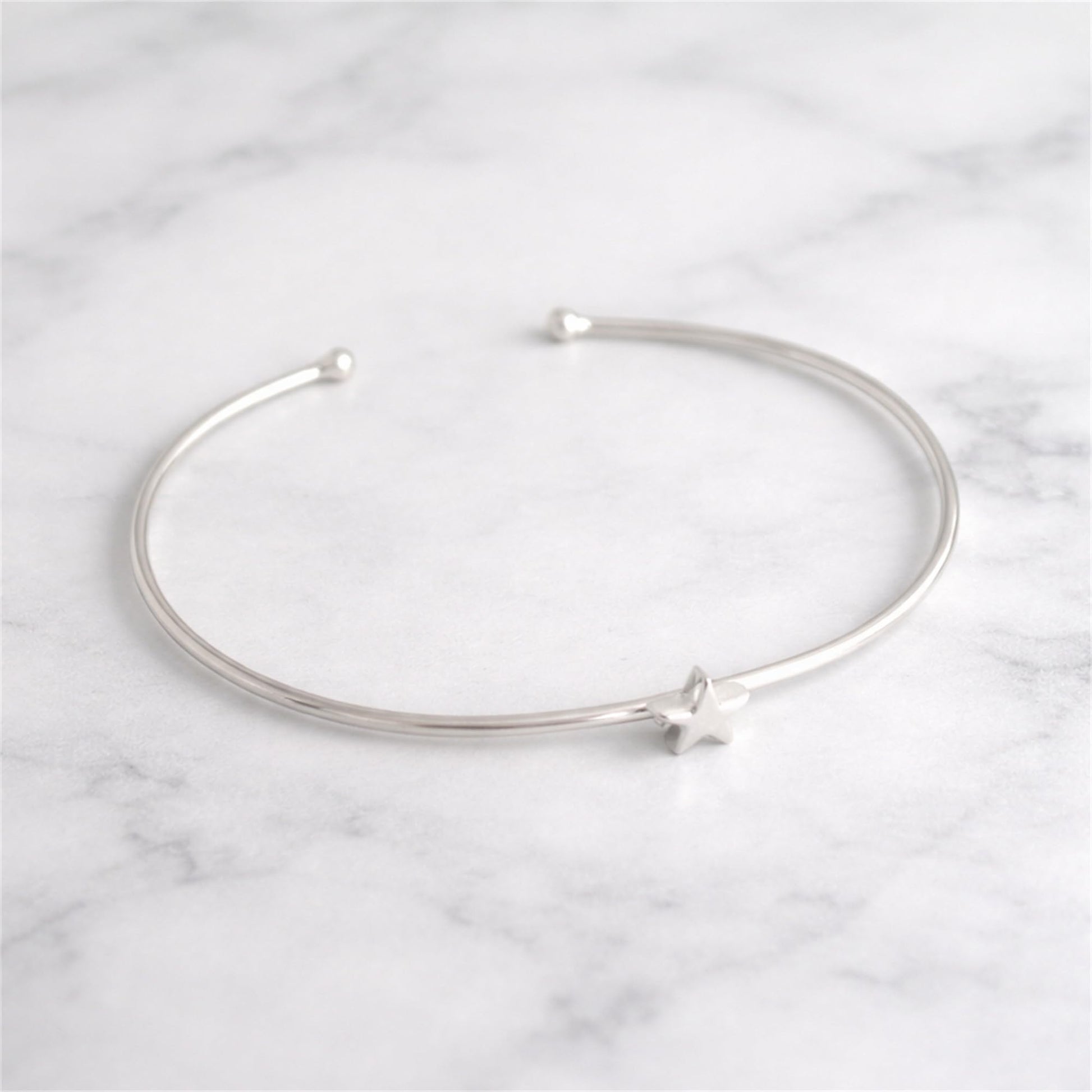 Star Bead Torque Bangle laid flat, silver-tone wire with star bead