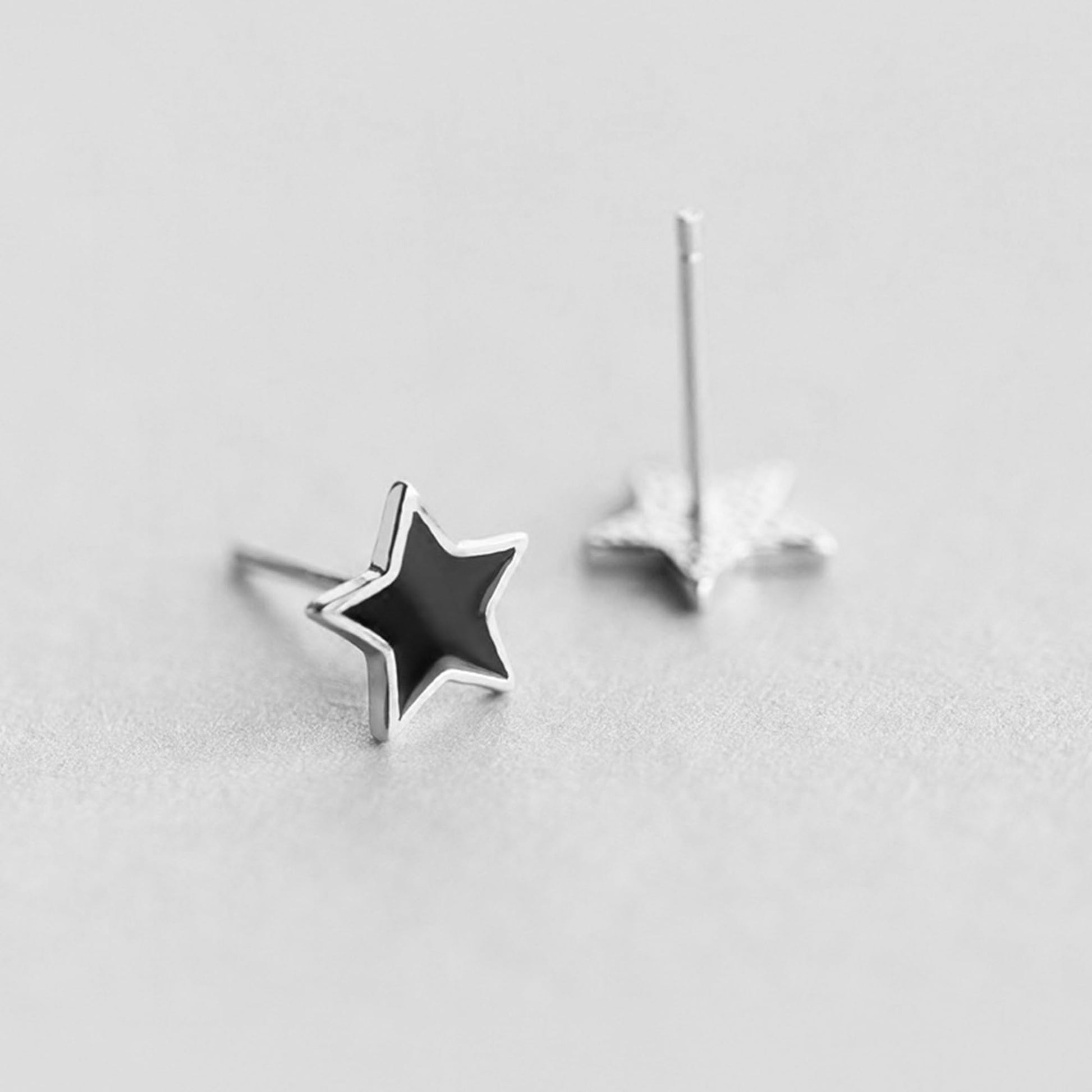 Black star stud earrings on silver posts, side view with one back visible
