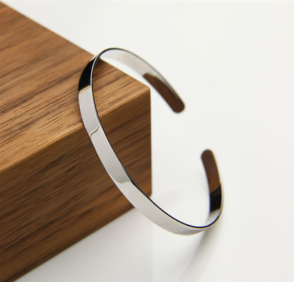 Polished cuff bangle on surface, shiny silver finish with curved open ends
