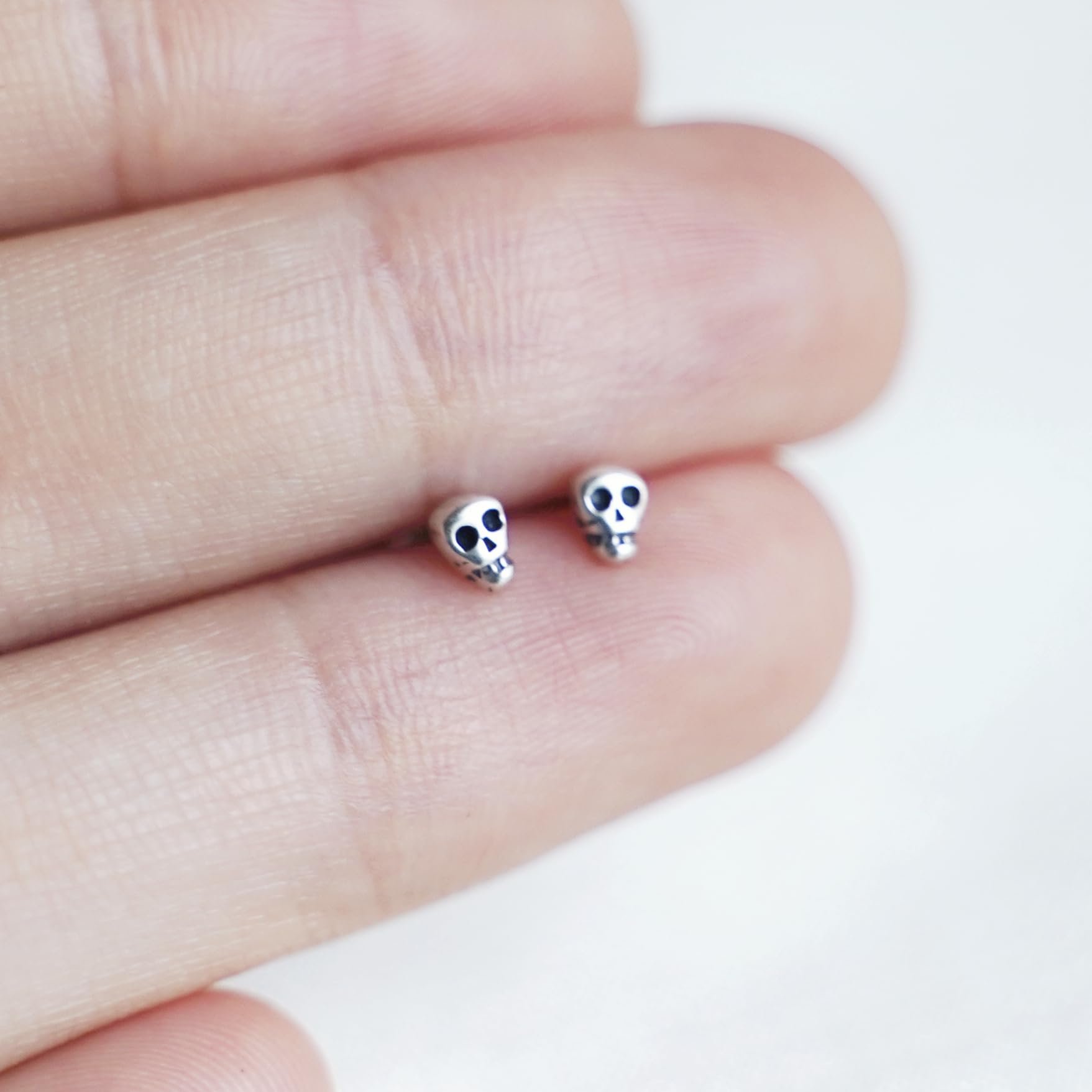 Two small skull stud earrings in hand; black-eyed skull faces on silver-tone studs