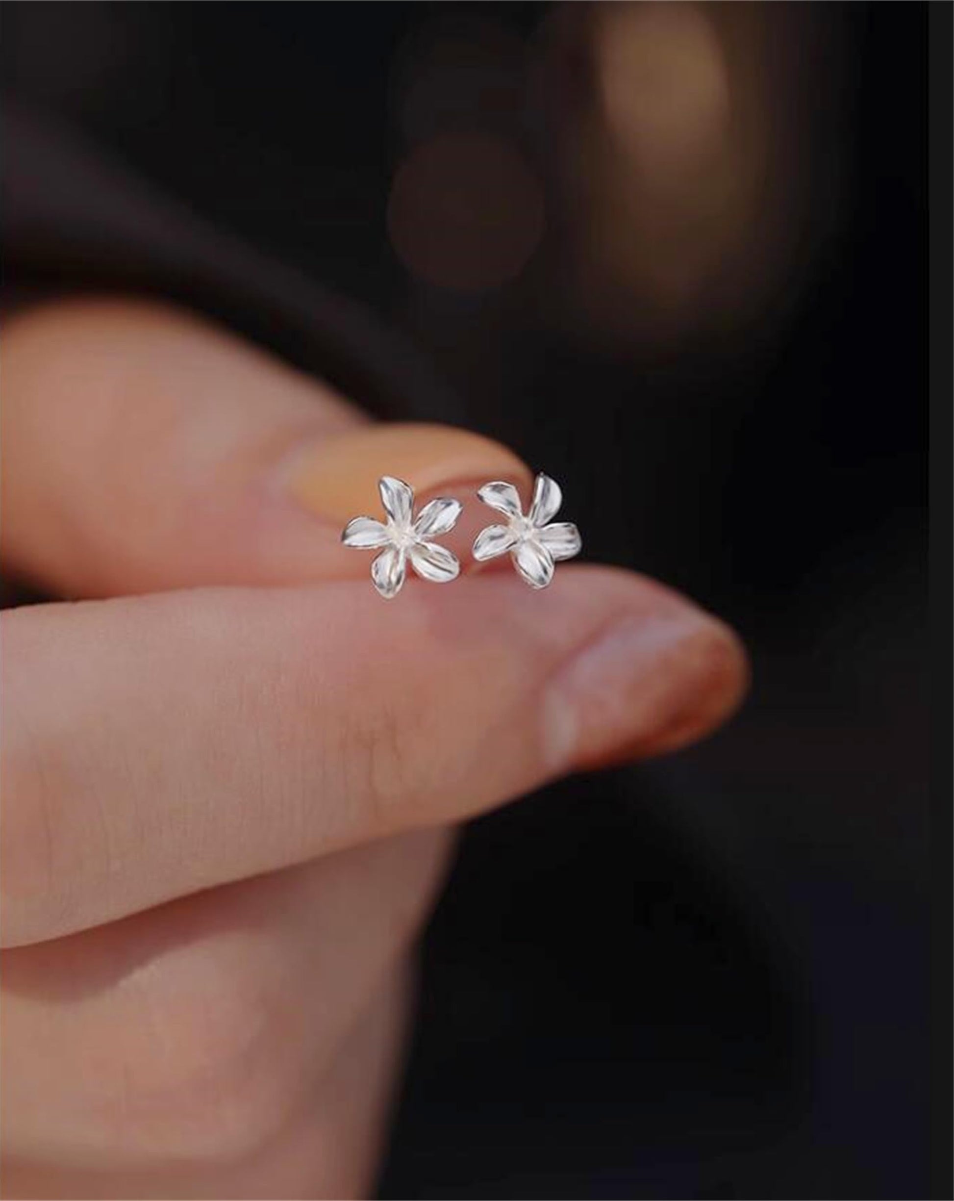Silver lily flower stud earrings held in hand, close-up