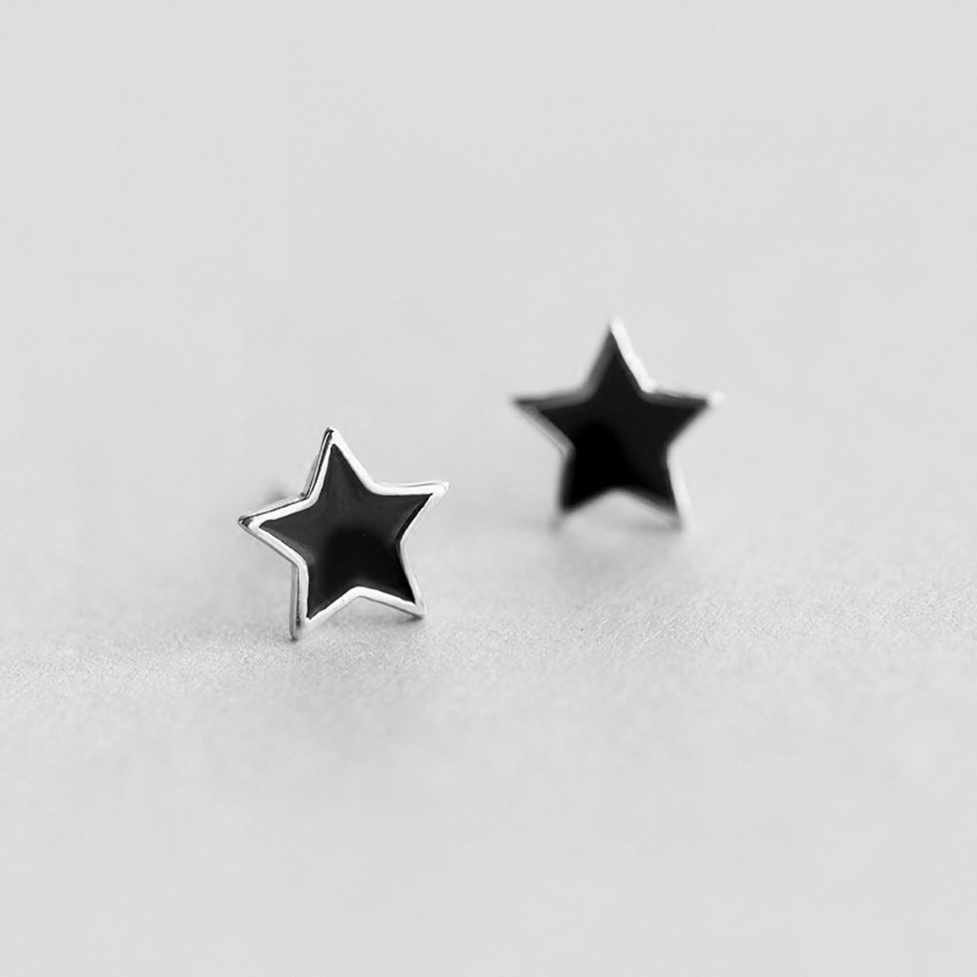 Black star studs with silver posts, angled view of both earrings