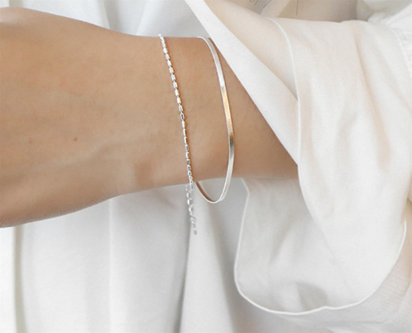 Layered snake bead bracelet on arm with multiple slender chain layers
