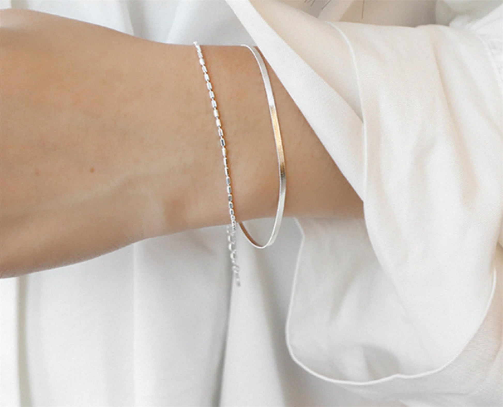 Layered snake bead bracelet on arm with multiple slender chain layers
