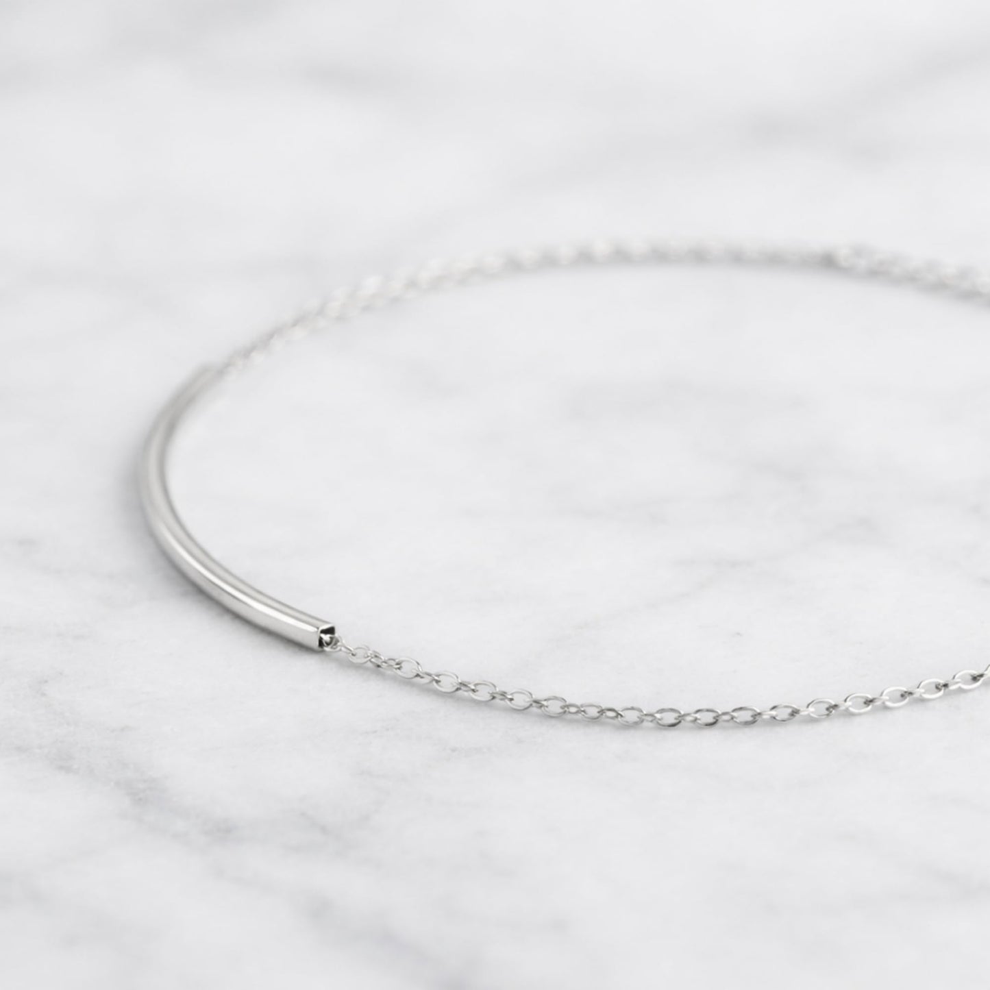 Curved Tube Curb Anklet close-up: curved tube bar with chain links and clasp