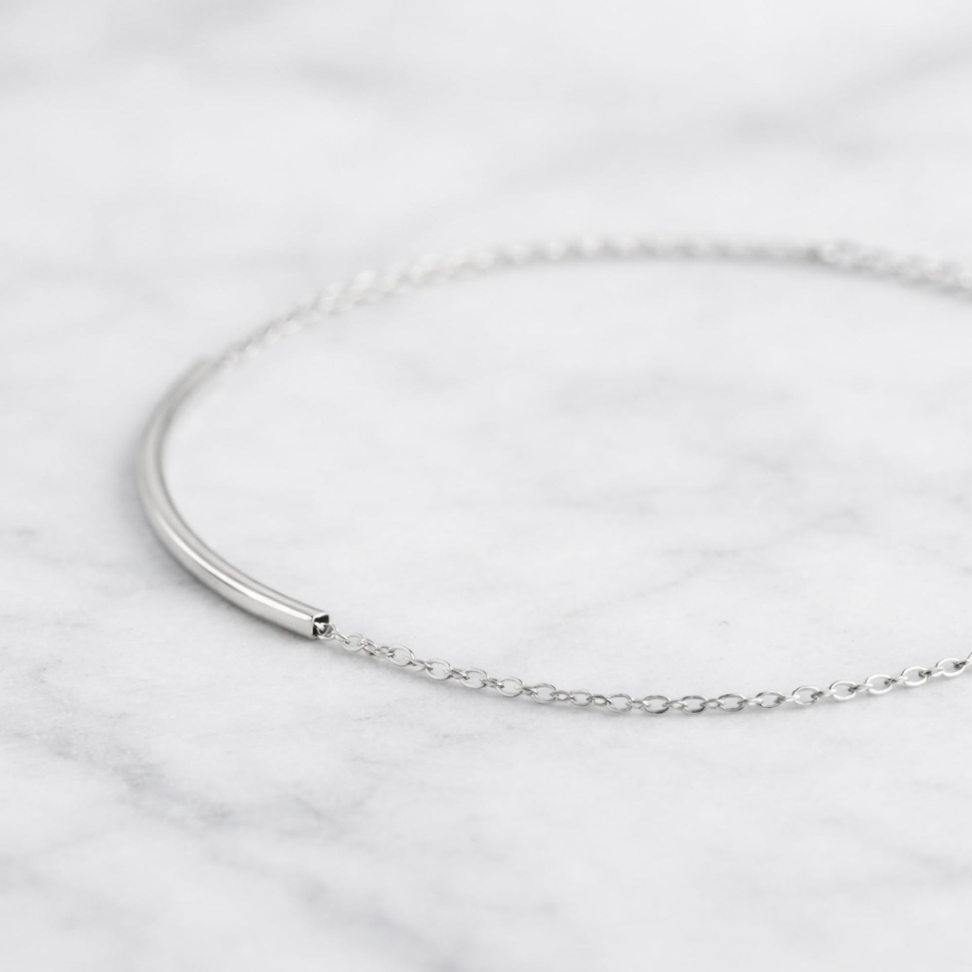 Curved Tube Curb Anklet close-up: curved tube bar with chain links and clasp