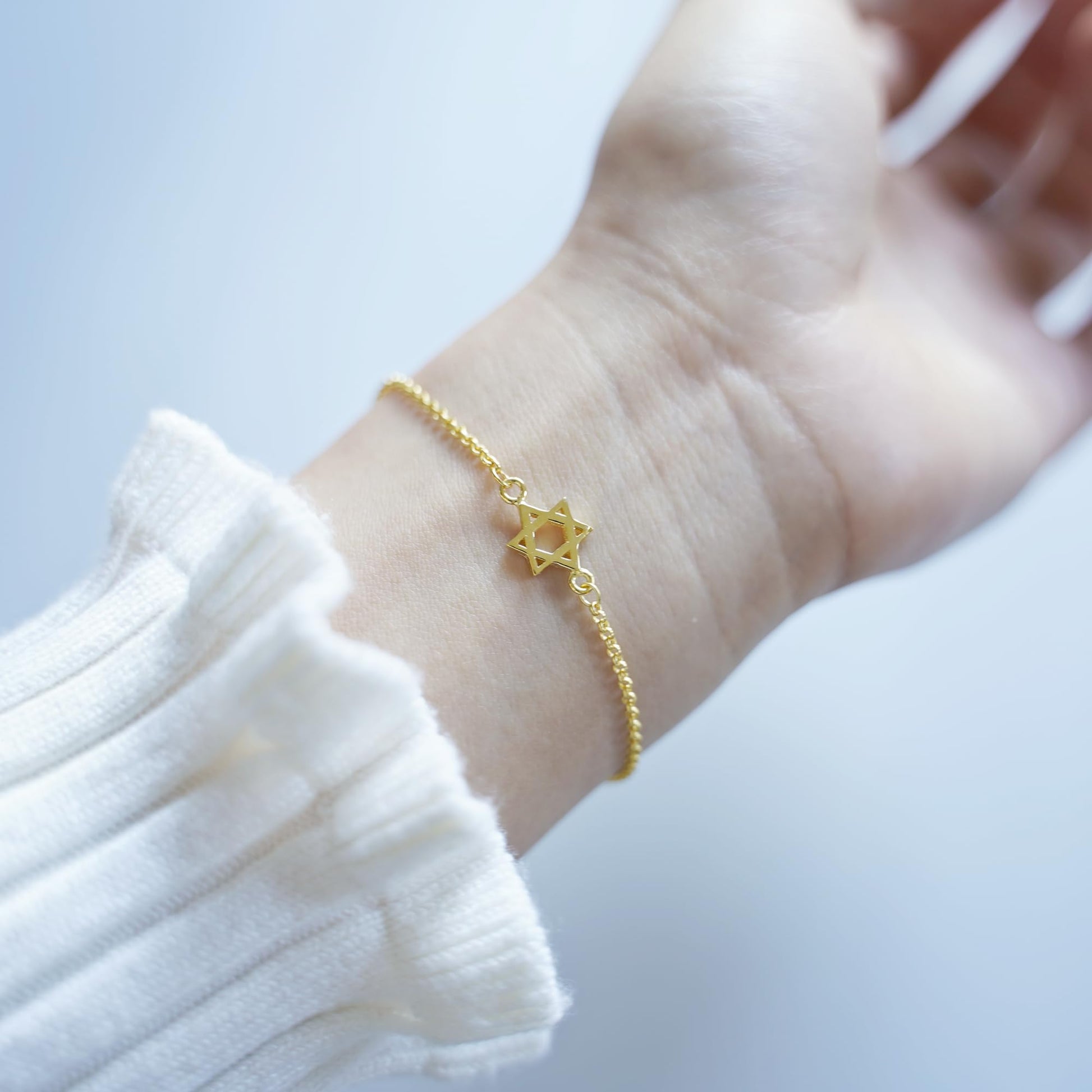 Gold Star of David bracelet on wrist with small star charm on chain.