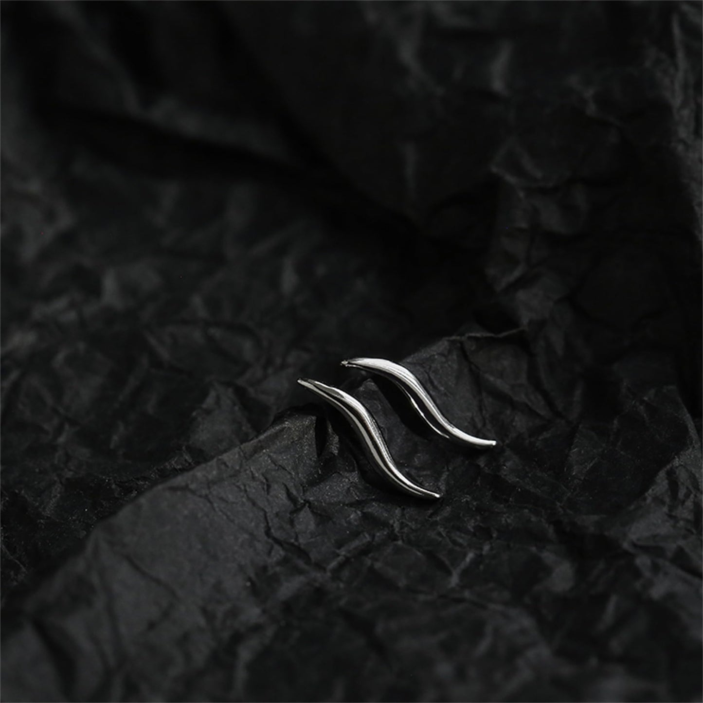 Wavy vine climber stud earrings, close-up of shiny curved vine-like wave shape