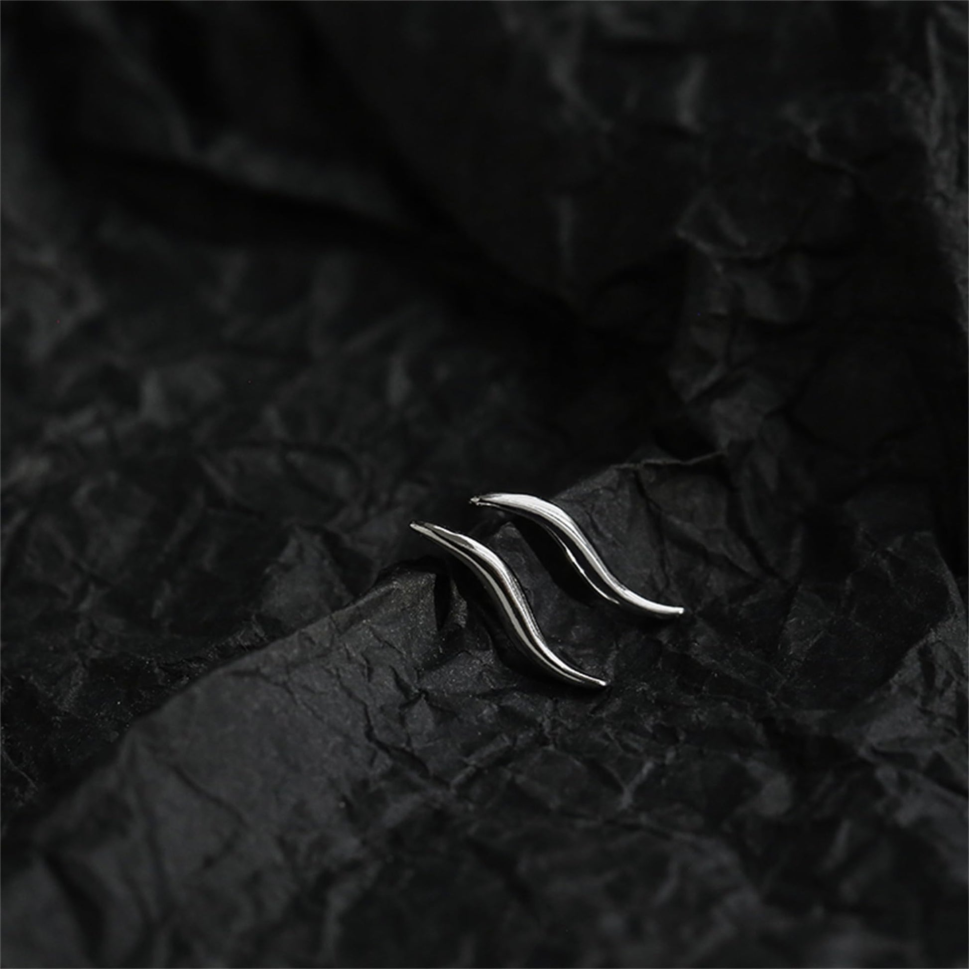 Wavy vine climber stud earrings, close-up of shiny curved vine-like wave shape