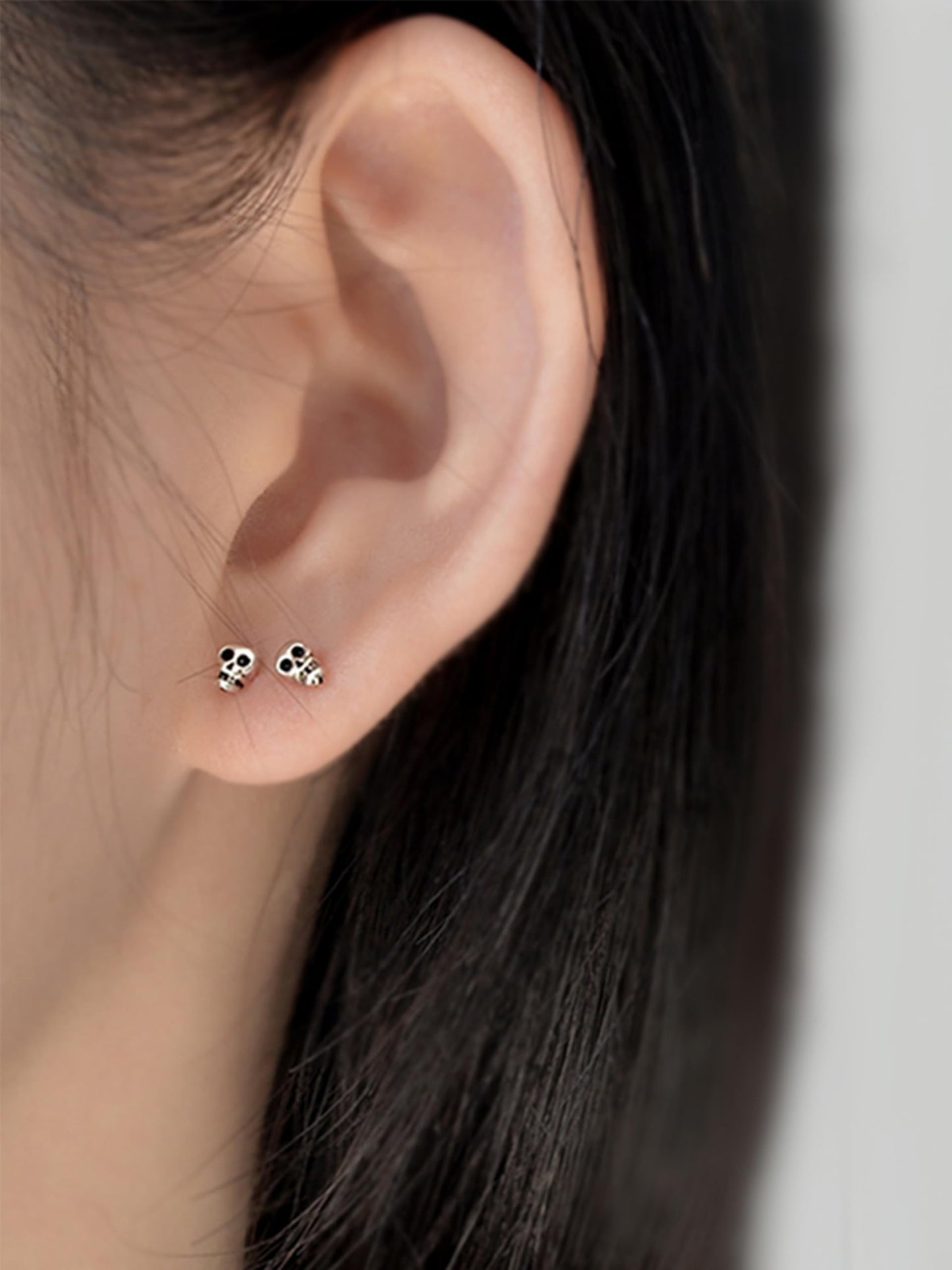 Skull stud earrings on ear; two mini black-eyed skull studs, silver-tone finish