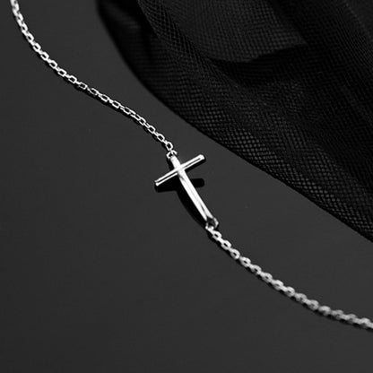 Close-up of sideways cross charm on silver-toned anklet chain