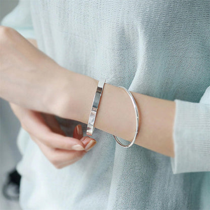 Polished cuff bangle worn on wrist, smooth silver-tone bracelet