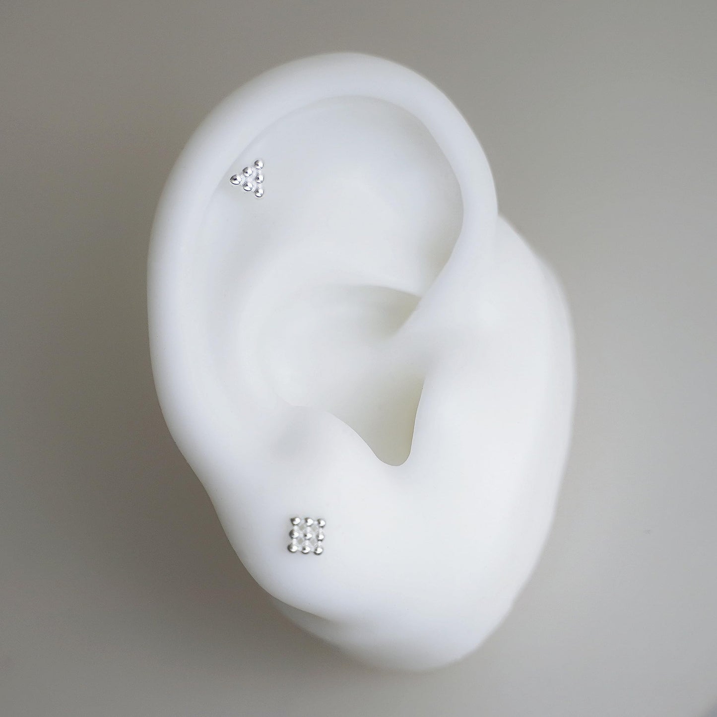 Mini geometric studs on ear-shaped holder: cube and triangle studs