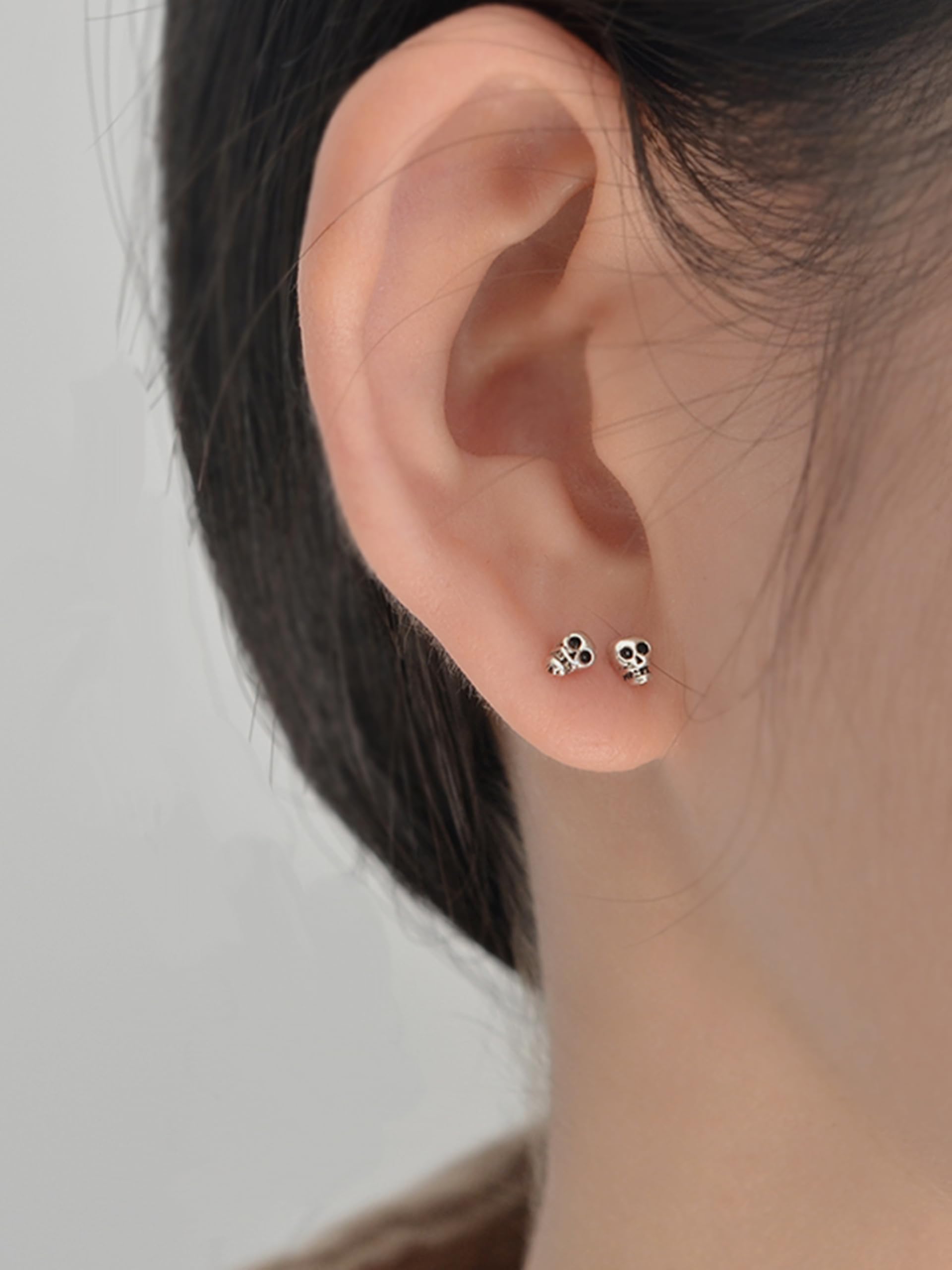 Mini gothic skull stud earrings on ear; small black-eyed skulls, silver-tone posts