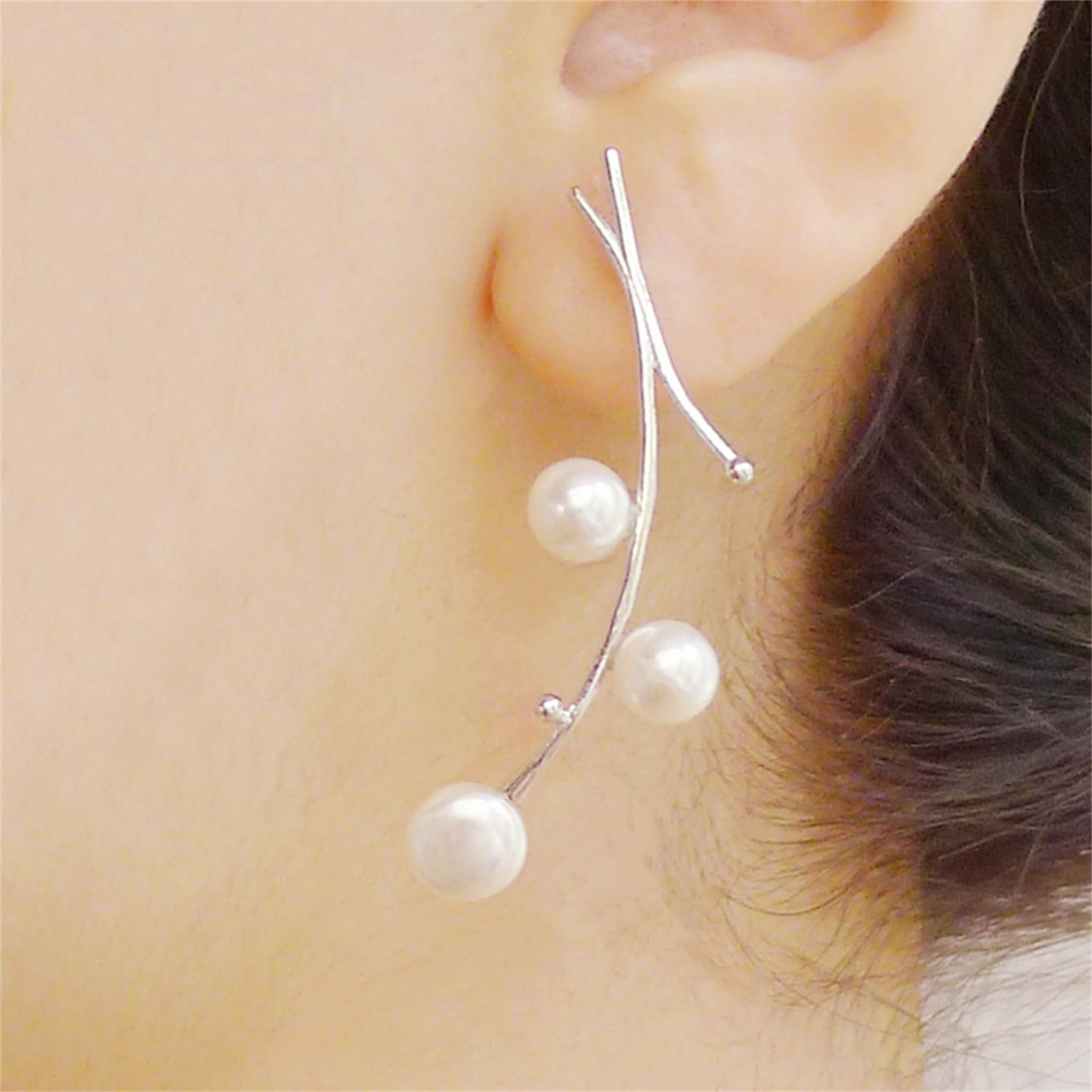 Close-up of pearl drop earrings: three white pearls on silver hooks