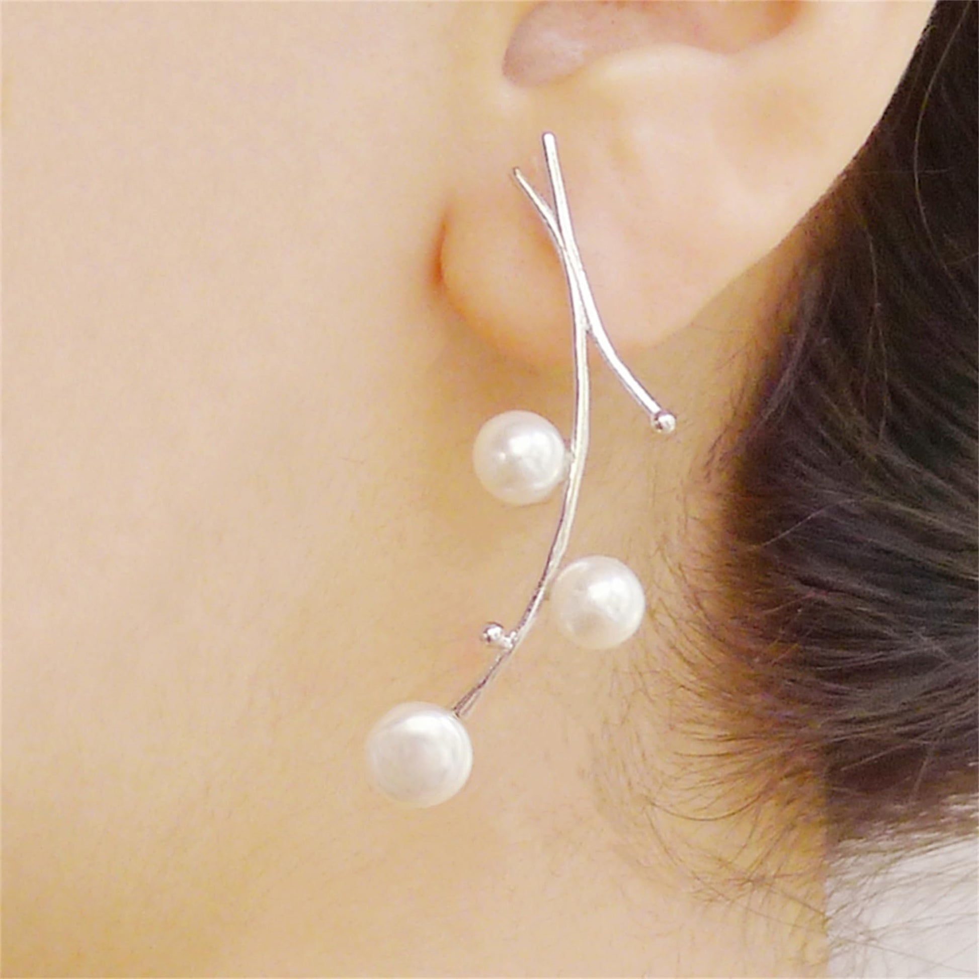 Close-up of pearl drop earrings: three white pearls on silver hooks