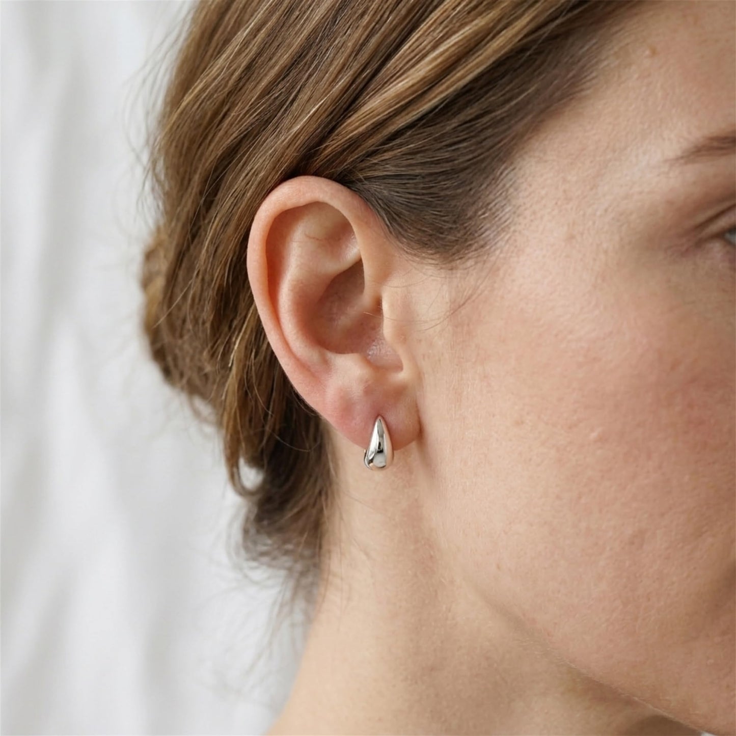 Silver teardrop hoop huggie earrings worn, small crescent hoop silhouette