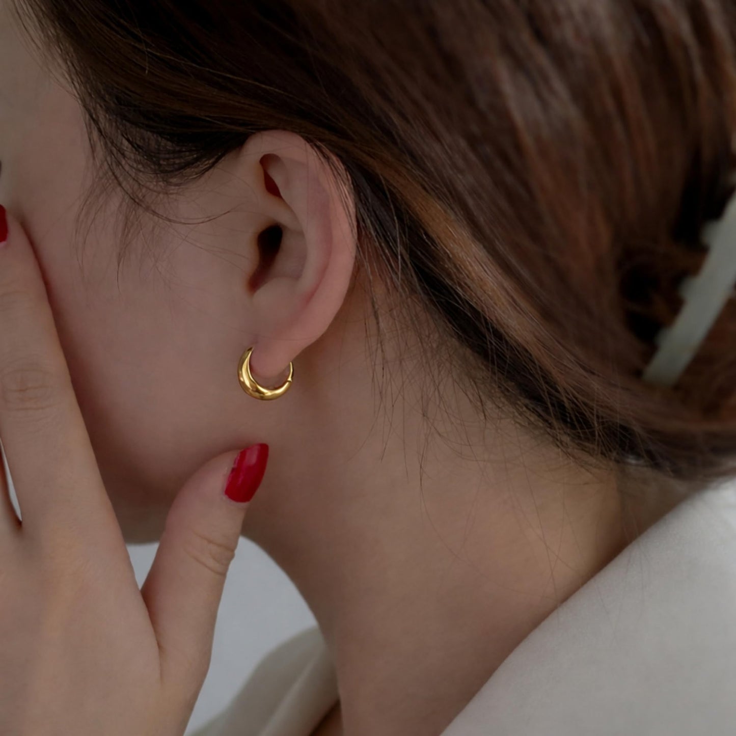 Gold teardrop hoop huggie earrings on ear, curved clasp and shine