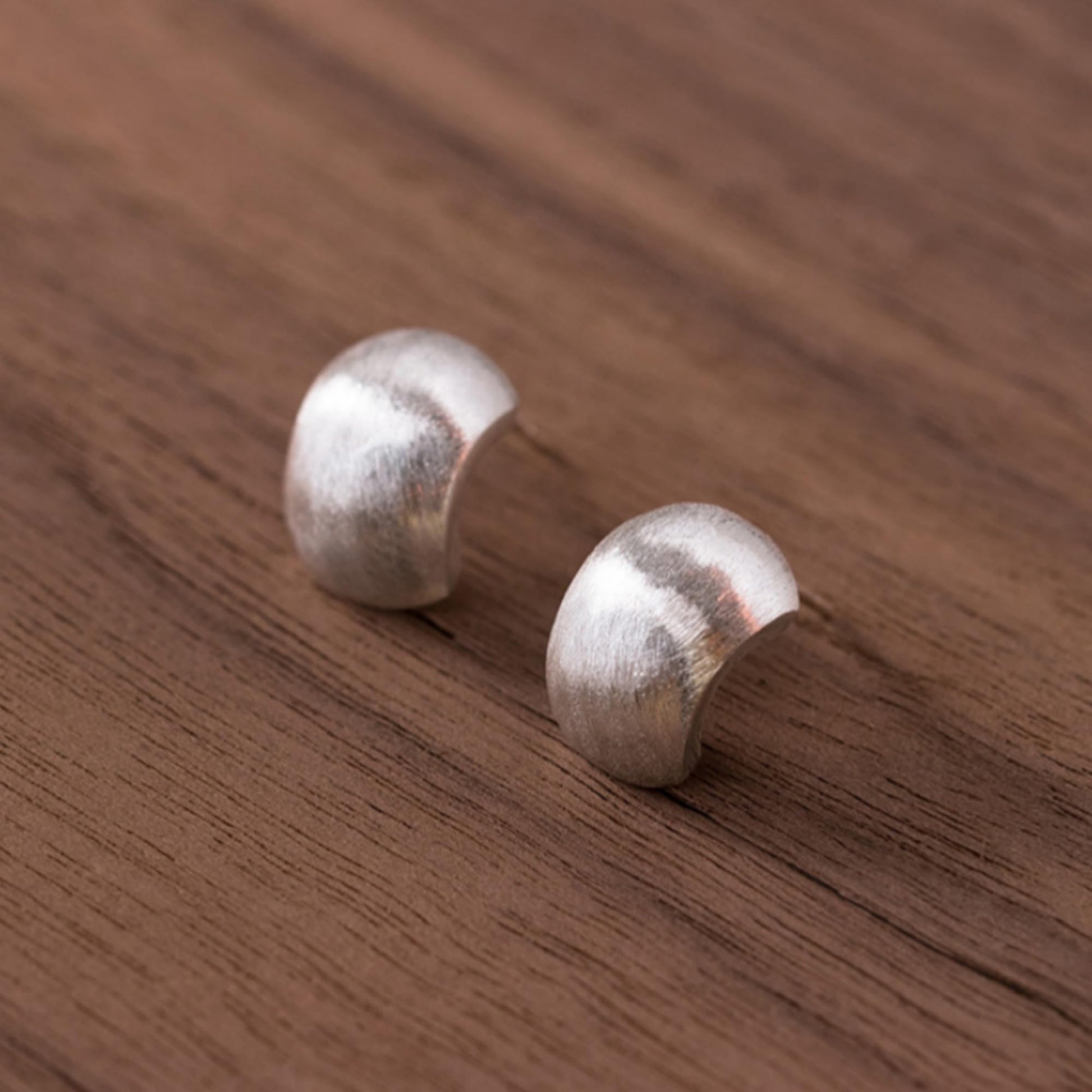 Brushed half-hoop drop earrings on flat surface, silver curved discs