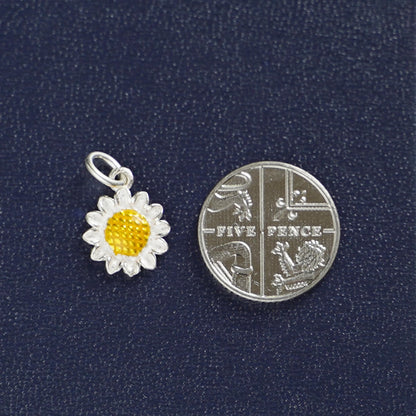 Colgante girasol amarillo y plateado, junto a moneda para mostrar el tamaño