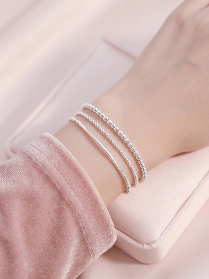 Stacked silver stretch bracelets with beaded strands and curved metal bars