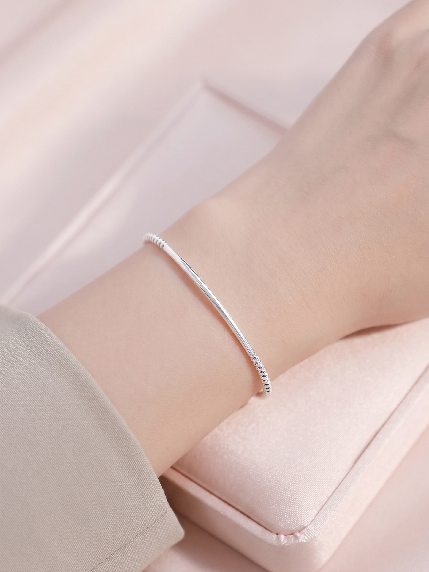 Silver beaded stretch bracelet on wrist with slim curved metal bar