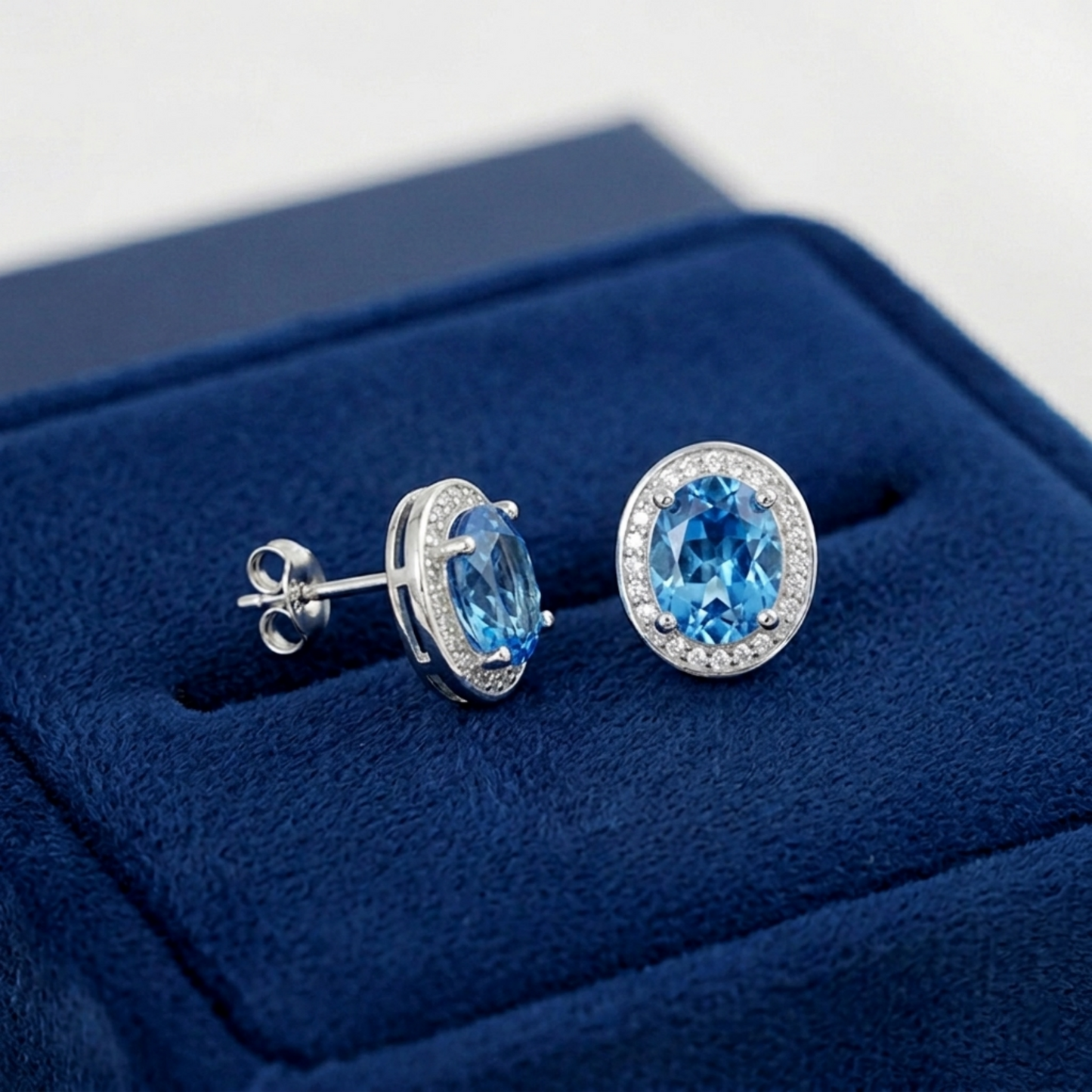 Blue topaz CZ halo studs, side view: oval blue stone in halo setting with visible posts.