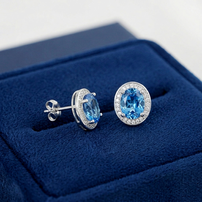 Blue topaz CZ halo studs, side view: oval blue stone in halo setting with visible posts.