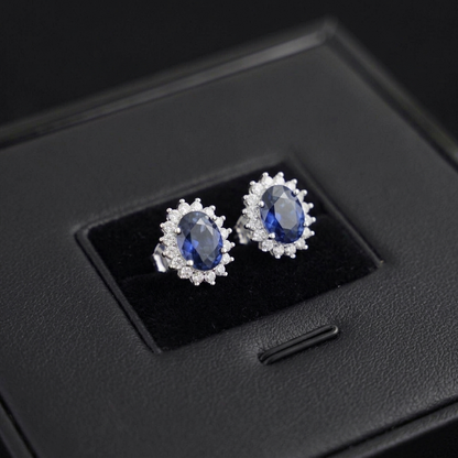 Sapphire oval stud cluster earrings with round white stone halo and prong setting, white metal