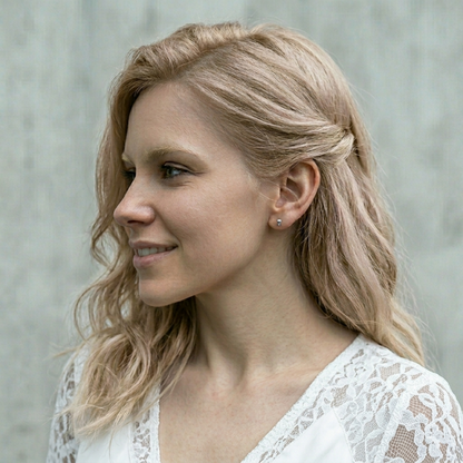 Person wearing mini skull stud earrings; small black-eyed skull studs, silver-tone finish